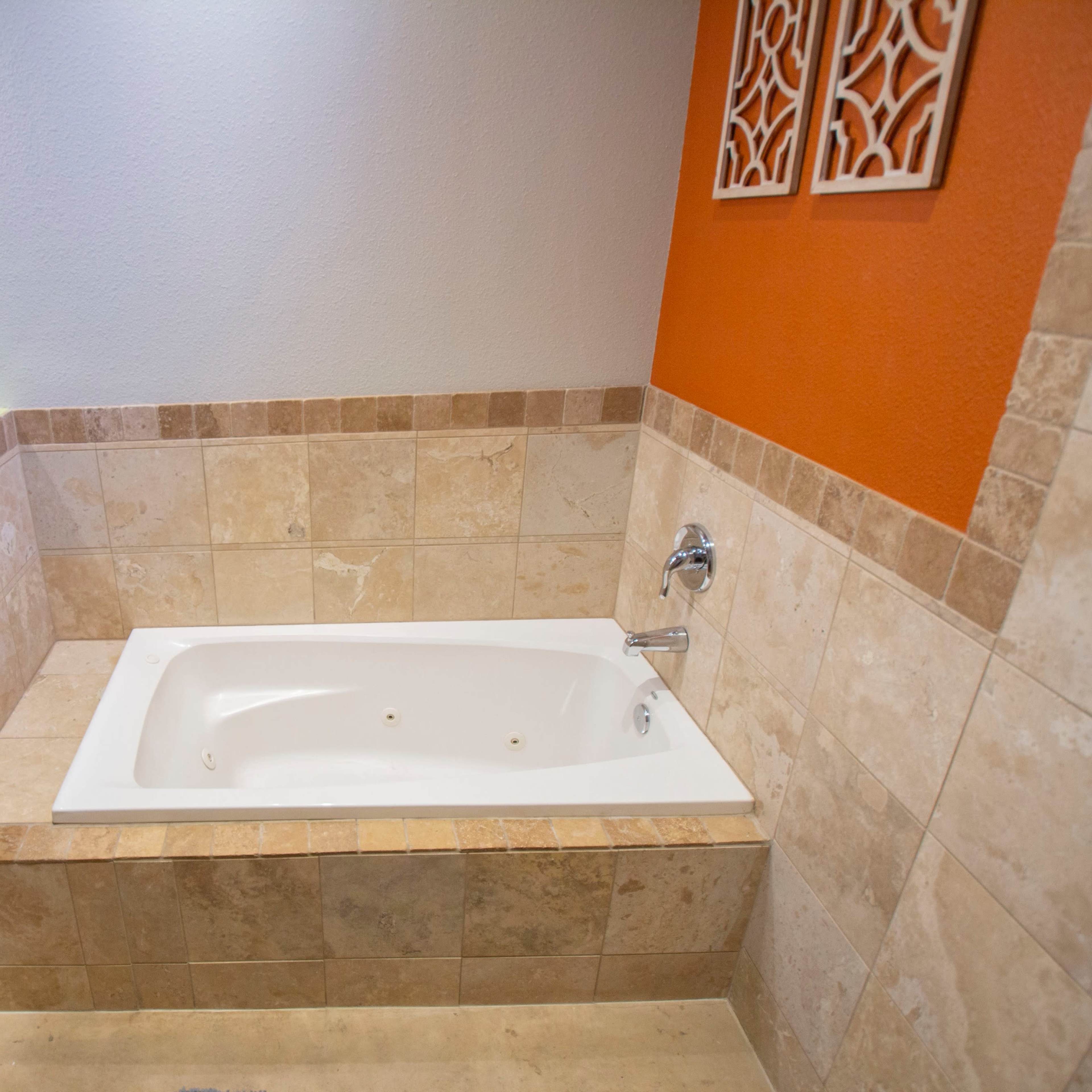 A jetted bathtub surrounded by tiled walls in a bathroom featuring a mix of orange and beige colors.