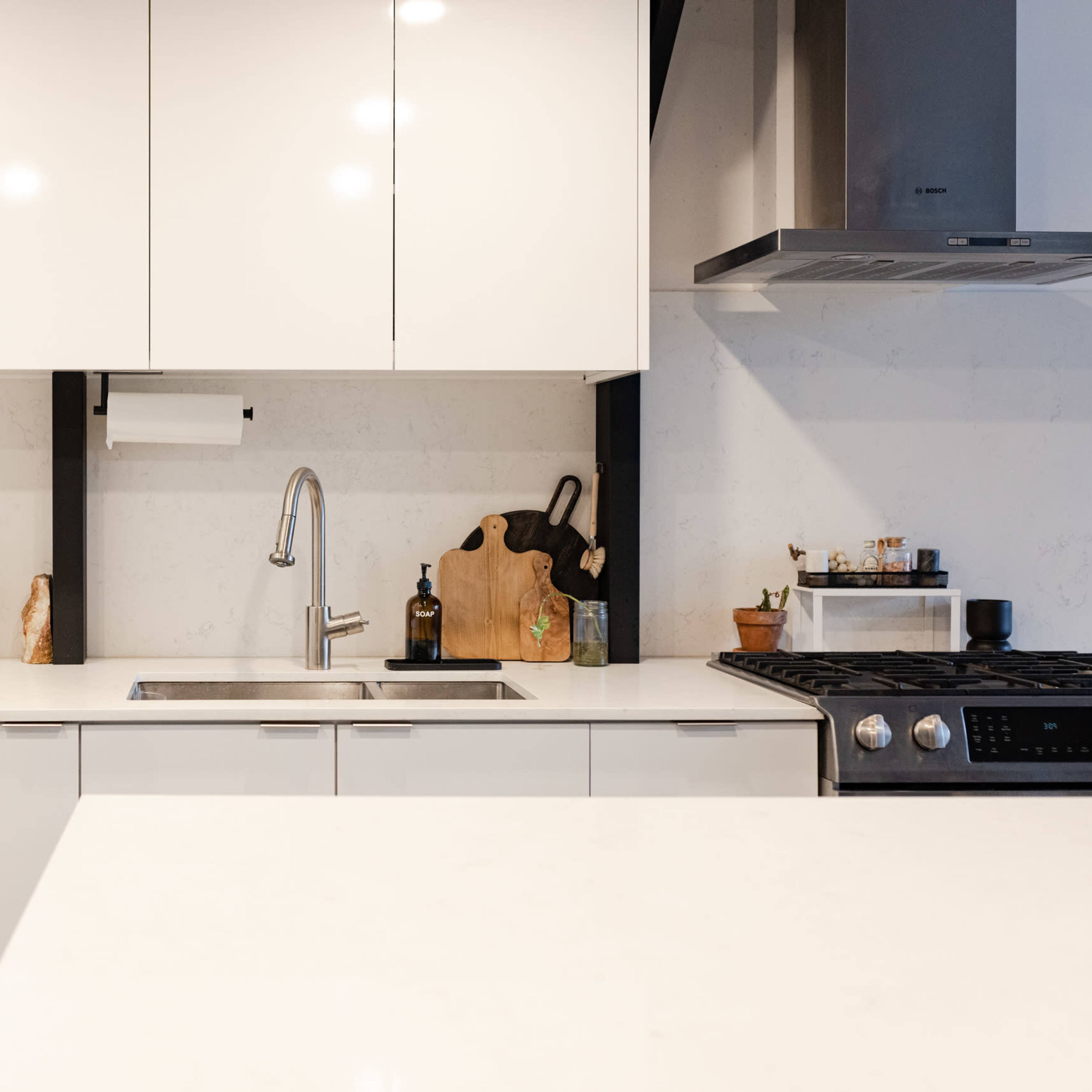 A modern kitchen with white cabinetry, a stainless steel dishwasher, a sink, and a gas stove.