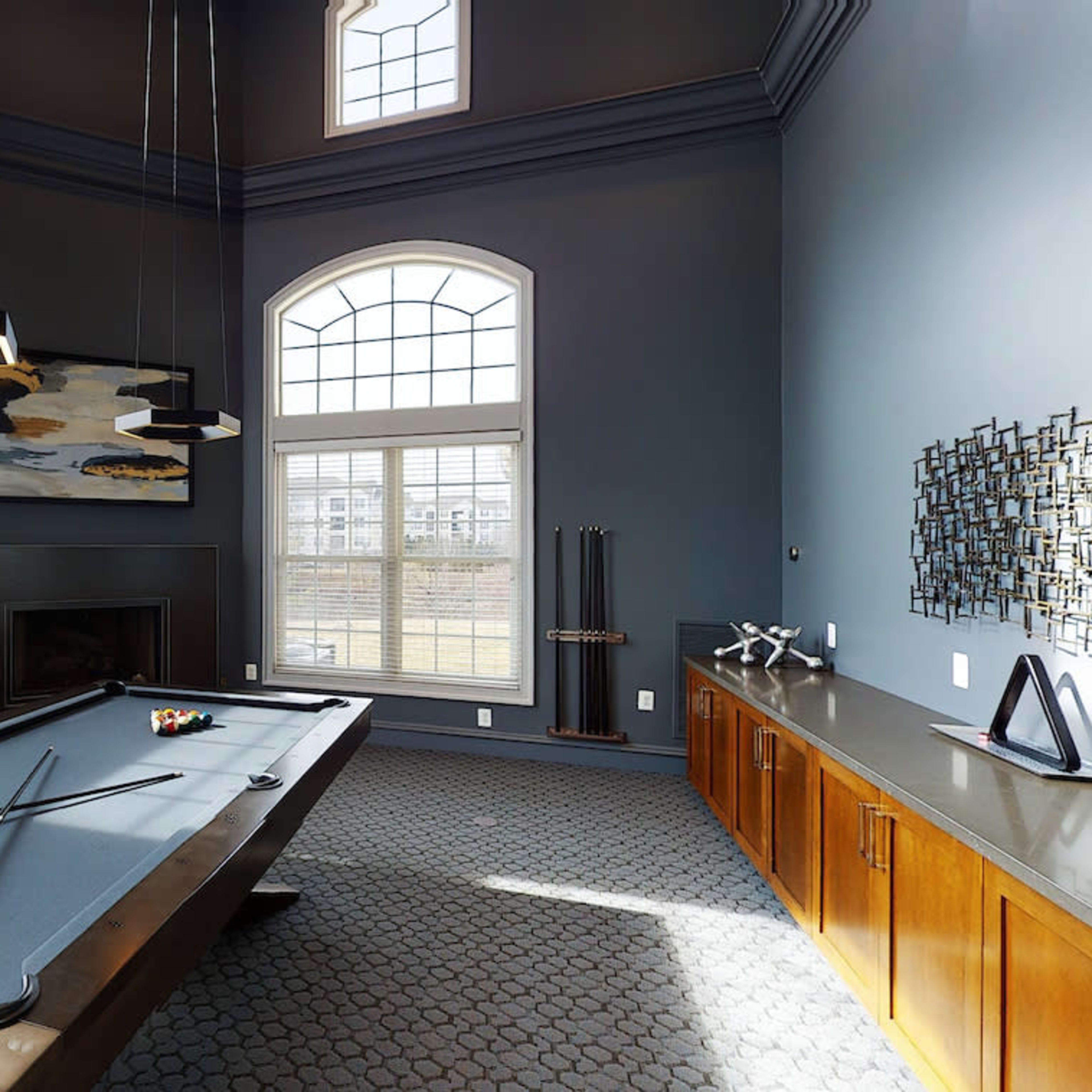 A spacious game room with a billiard table, tall windows, and modern furnishings.