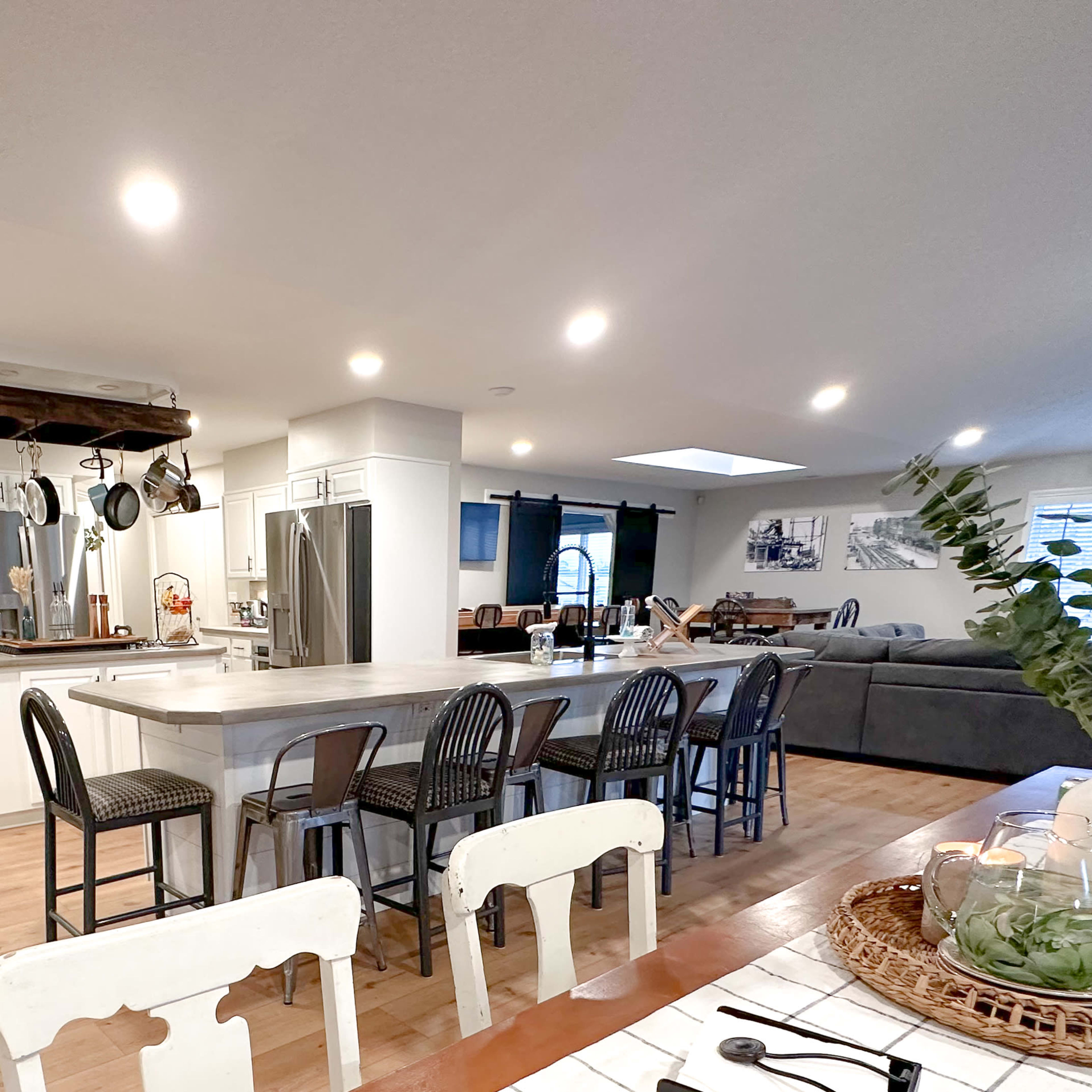 A spacious, modern kitchen with an island, bar stools, and open access to a living area furnished with a couch and decorative elements.