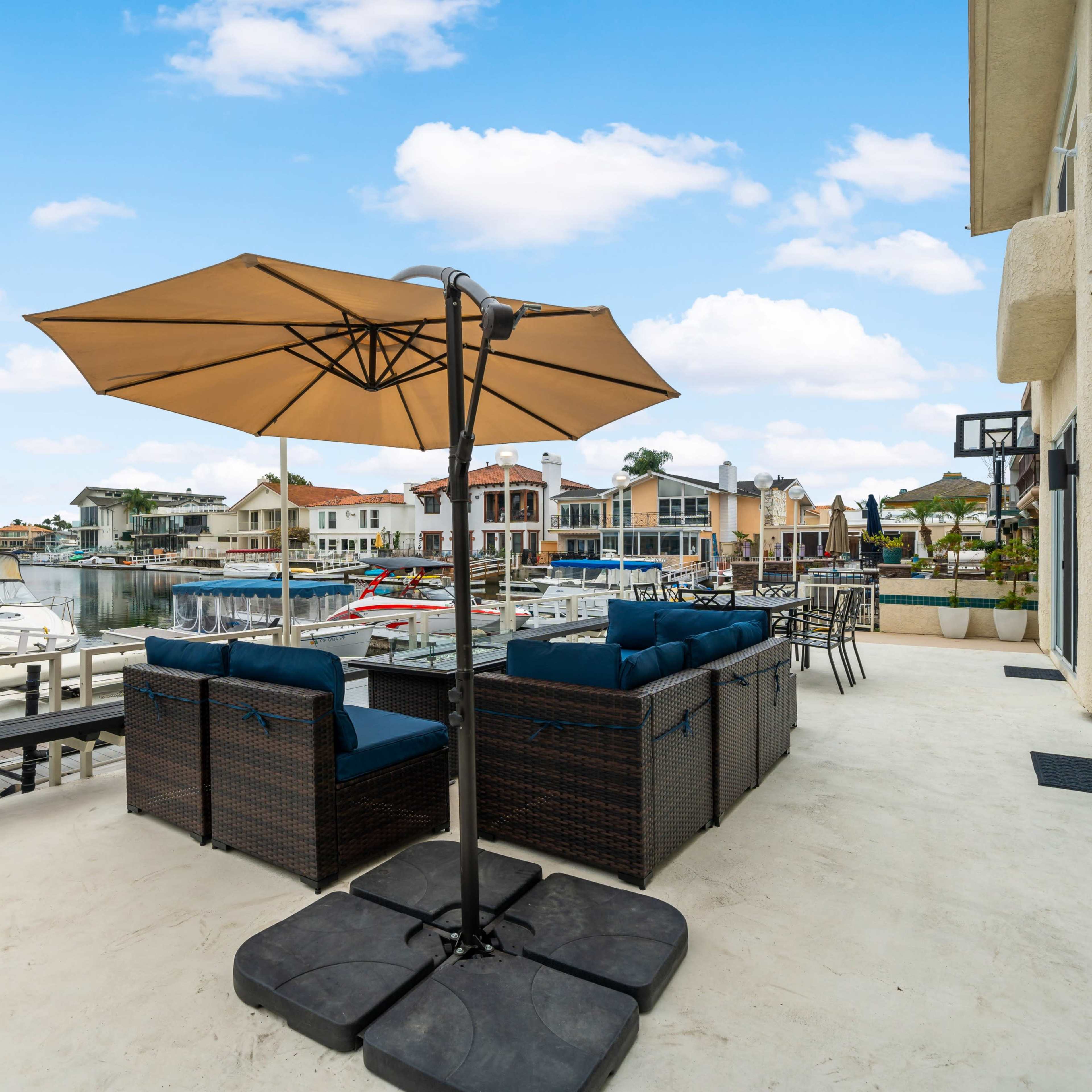 A patio with a large umbrella and outdoor seating overlooks a marina filled with boats and waterfront homes.