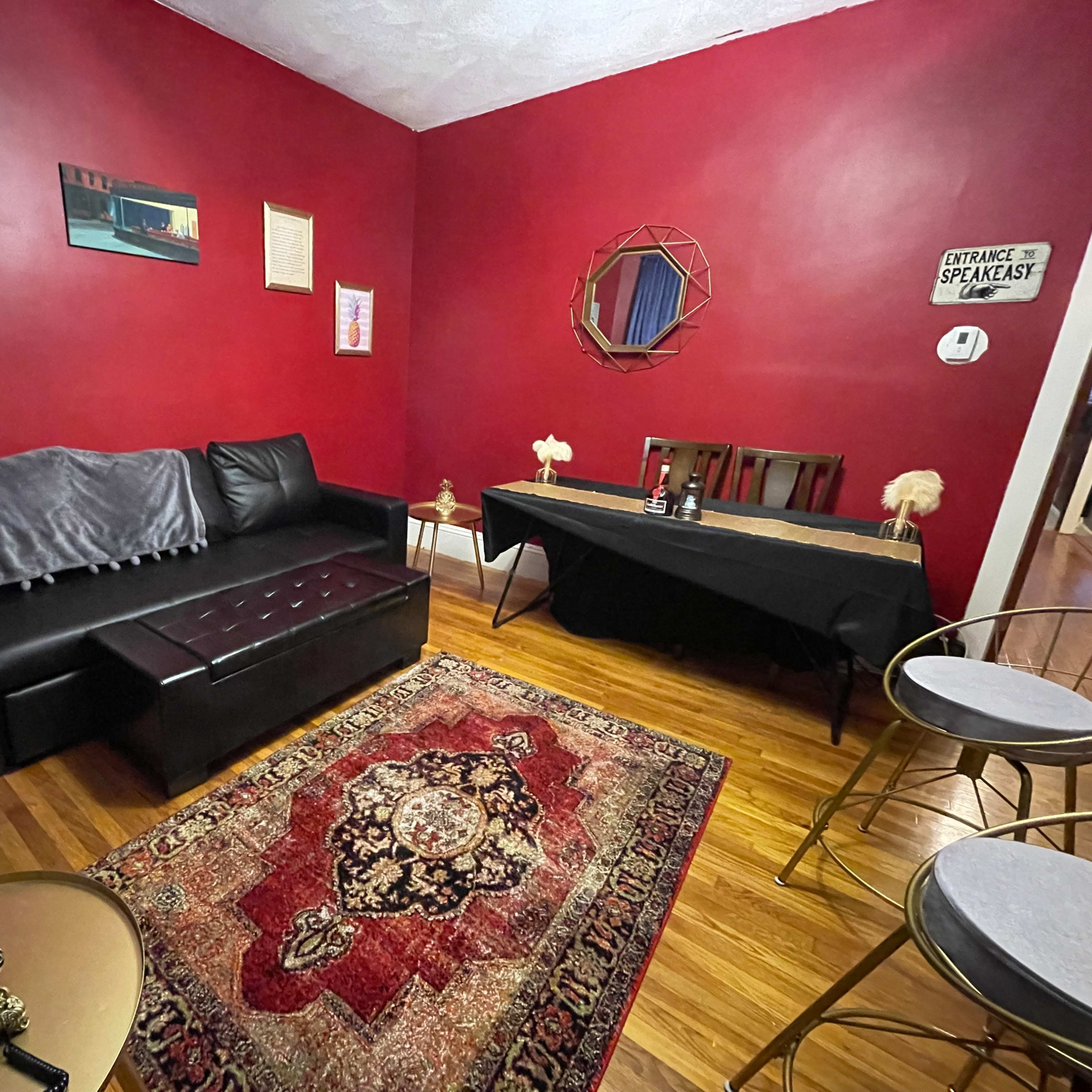A living room with red walls, a black couch, a wooden dining table, and an ornate rug.