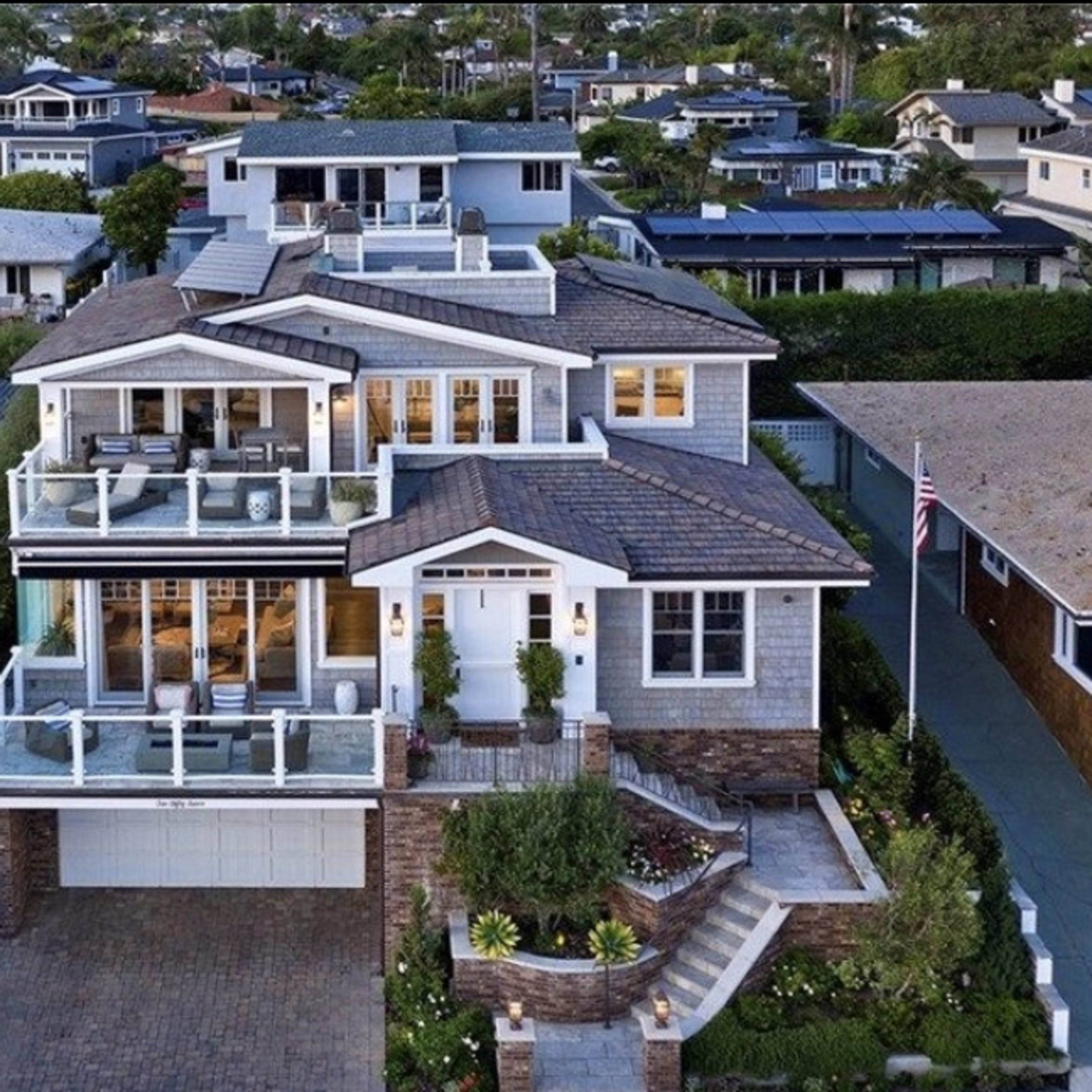 A modern house with multiple balconies, surrounded by other residential buildings and greenery.