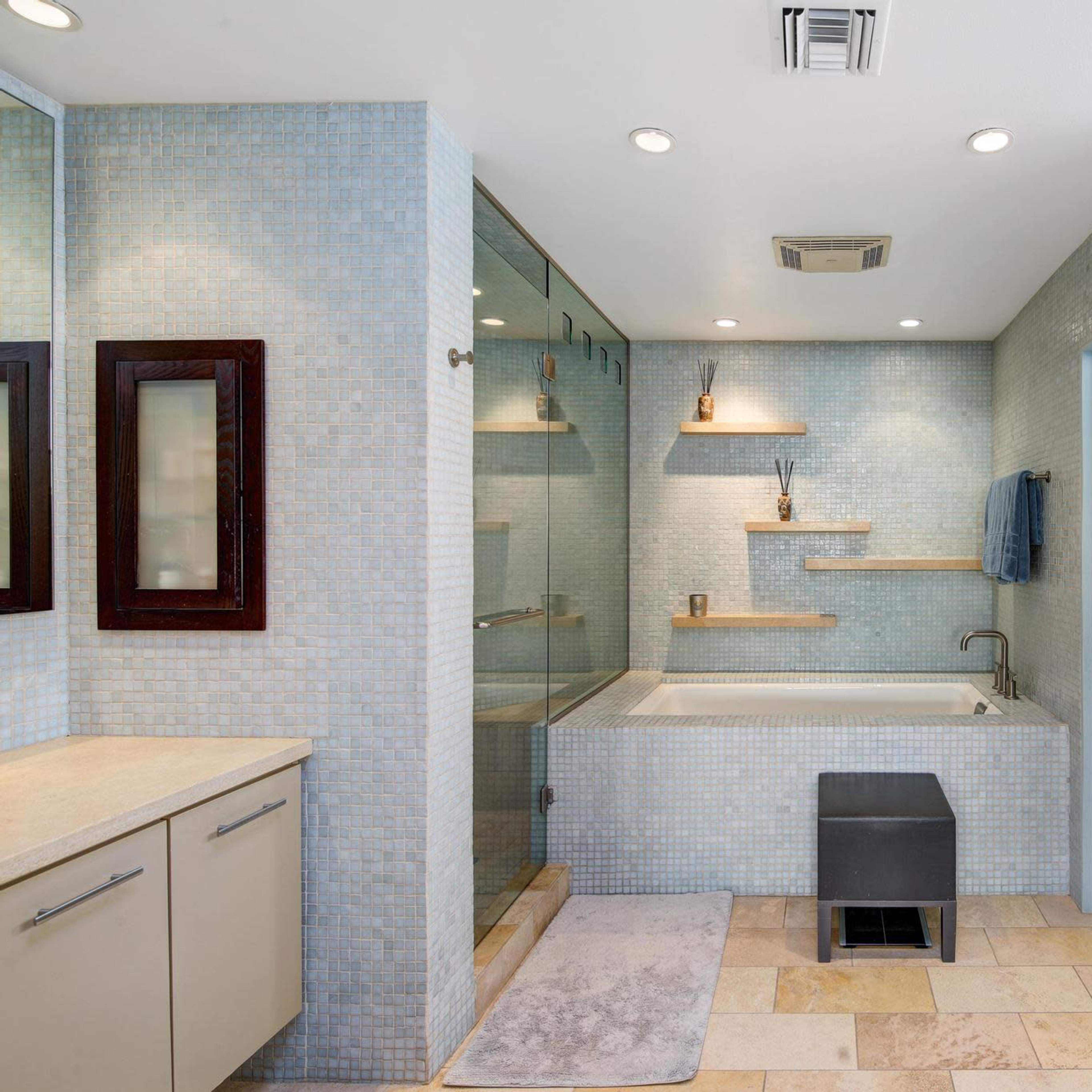 The bathroom features a glass shower enclosure, a soaking tub, dual vanities with storage, and mosaic tile walls.