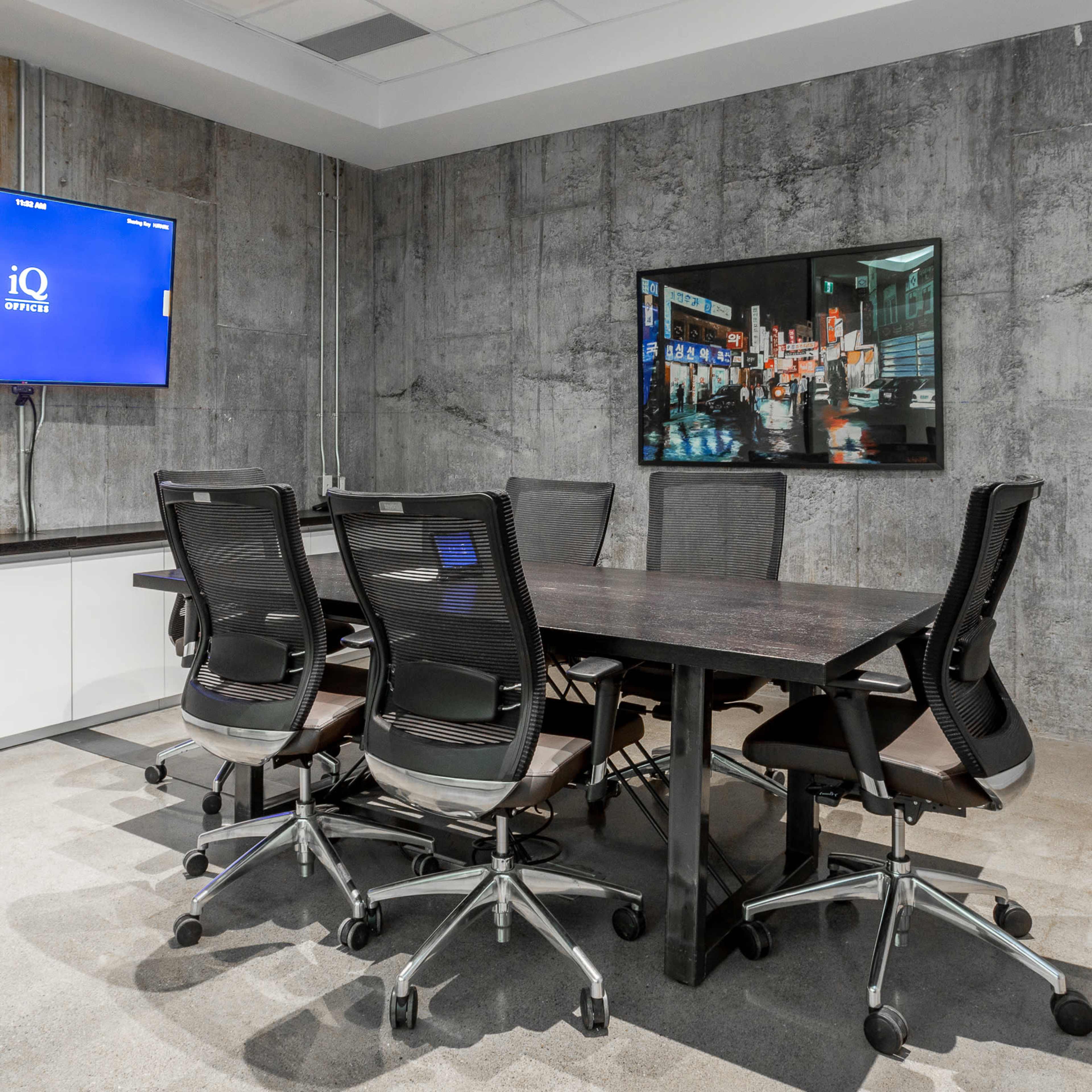 A modern conference room features a large wooden table surrounded by ergonomic chairs and a wall-mounted TV.