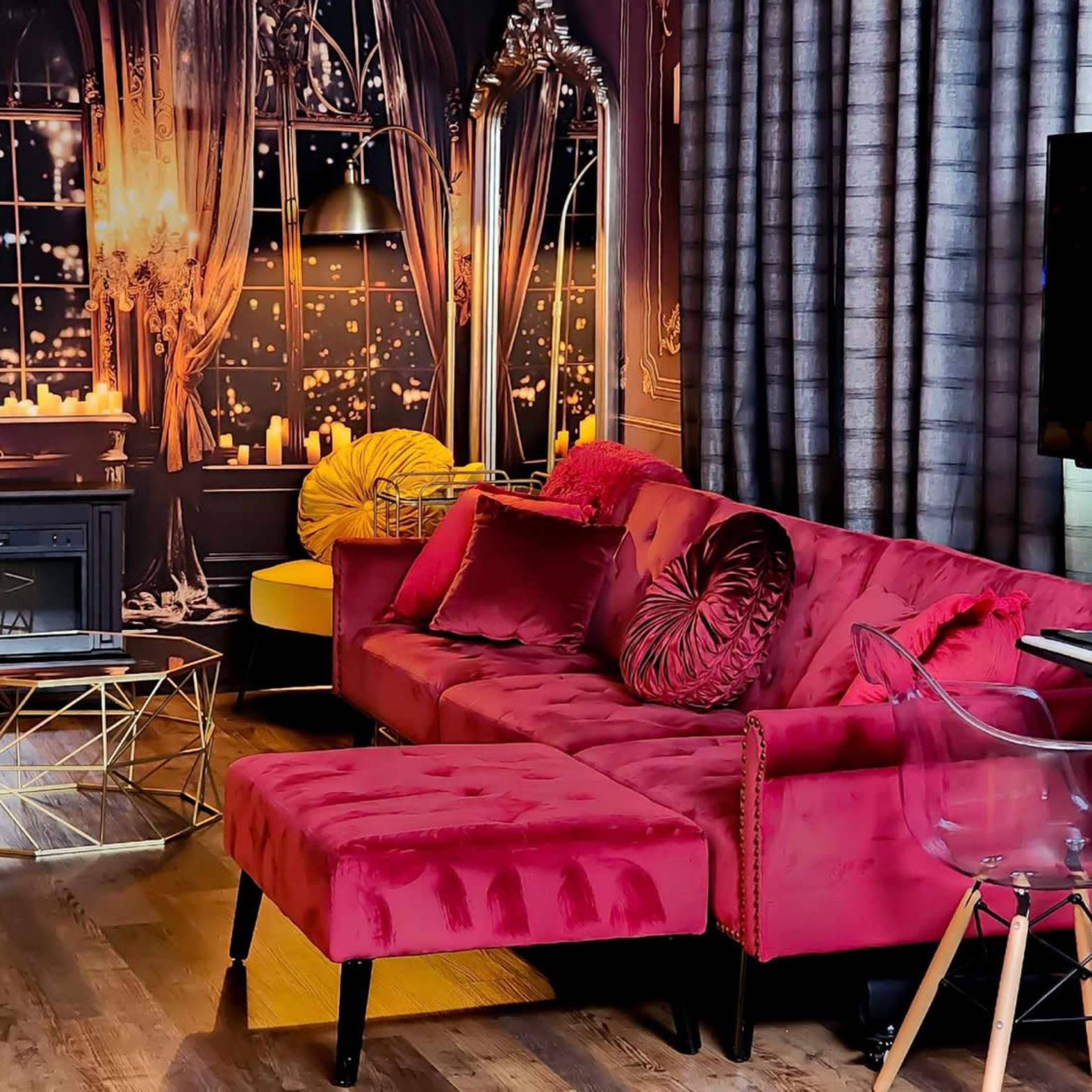 A lavish living room with a pink velvet sectional sofa, a glass coffee table, and a backdrop featuring a large window with city lights and candles.