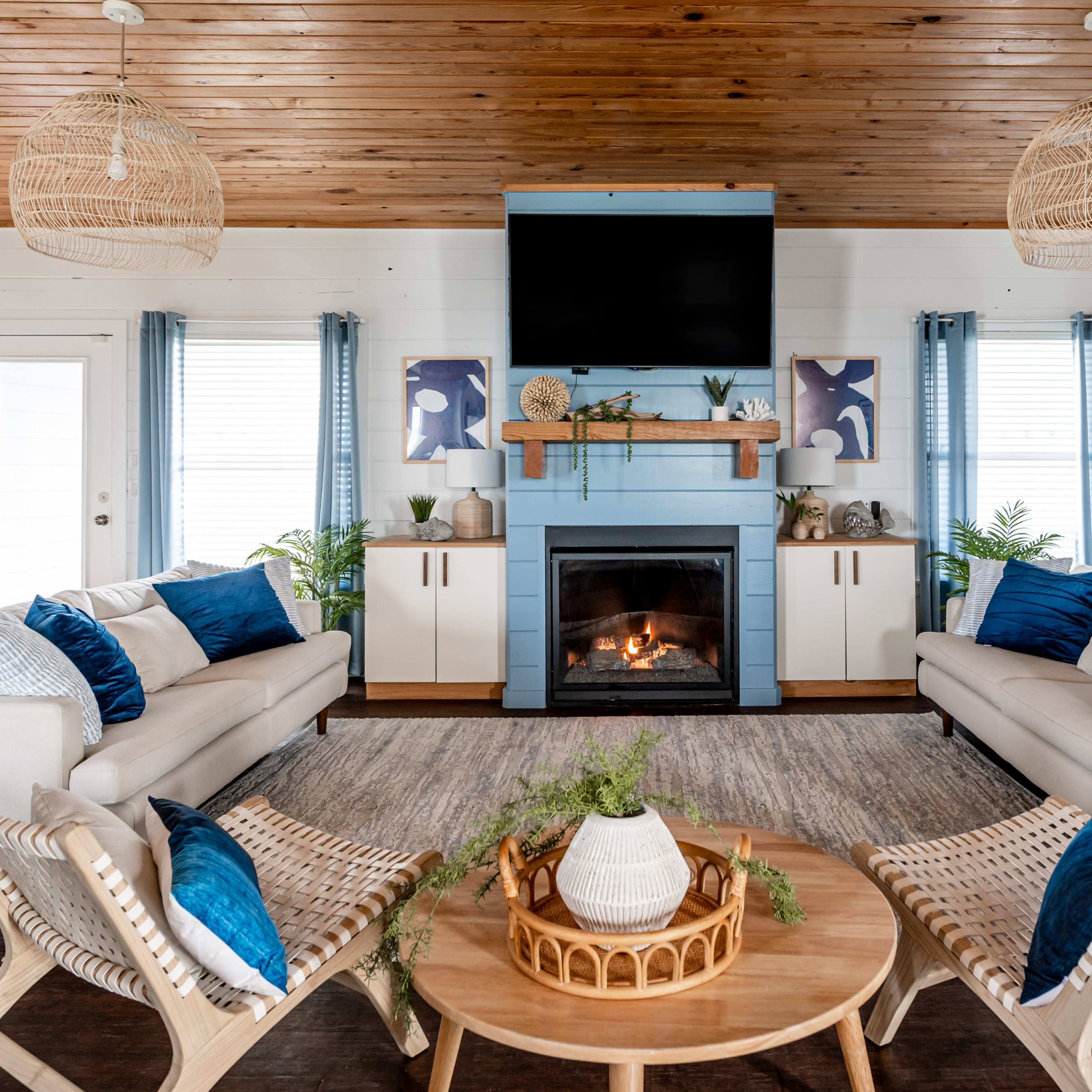 A modern living room with two sofas, a coffee table, a fireplace, and decorative plants, all surrounded by wooden paneling and large windows.