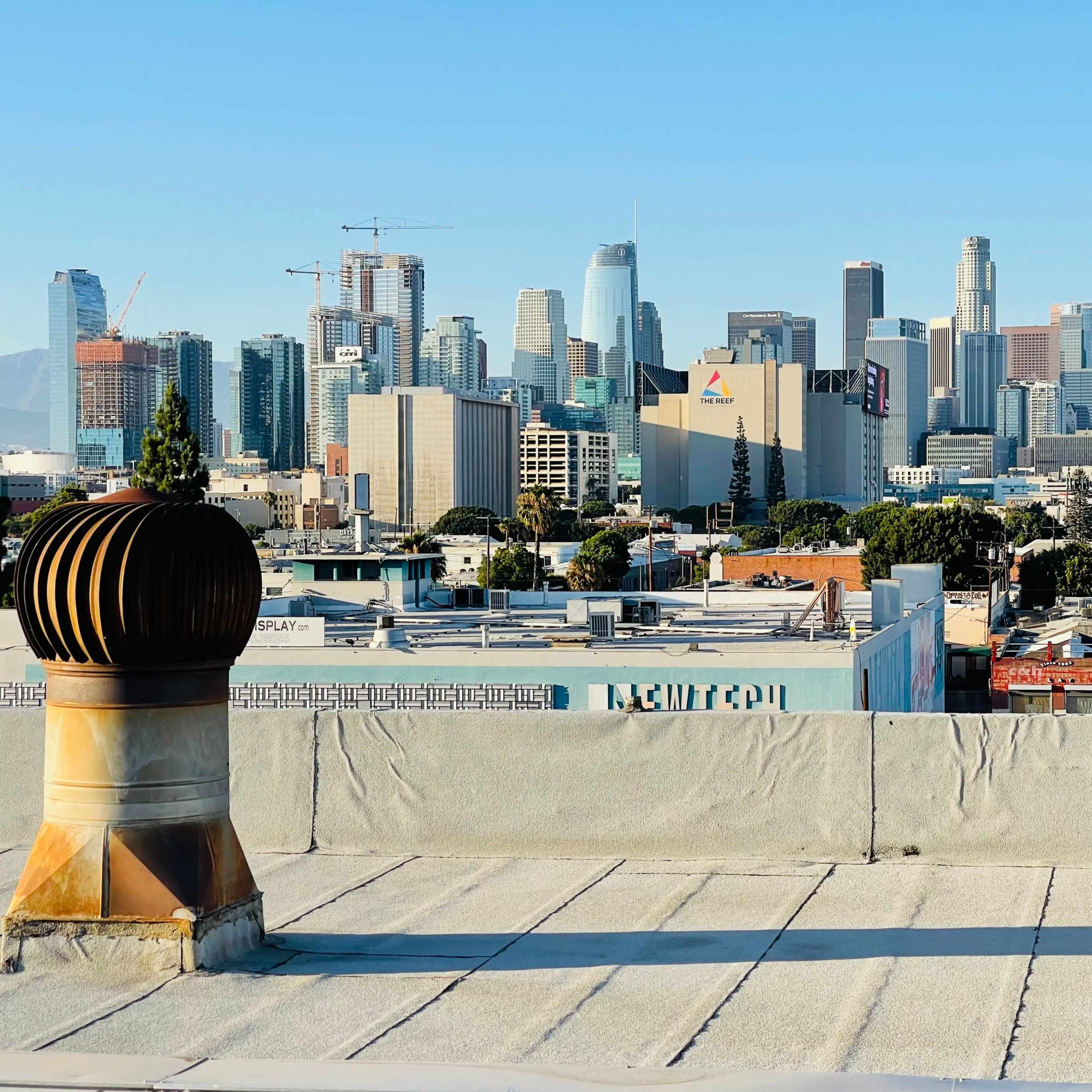 A rooftop view of downtown Los Angeles with skyscrapers in the background and industrial buildings in the foreground.