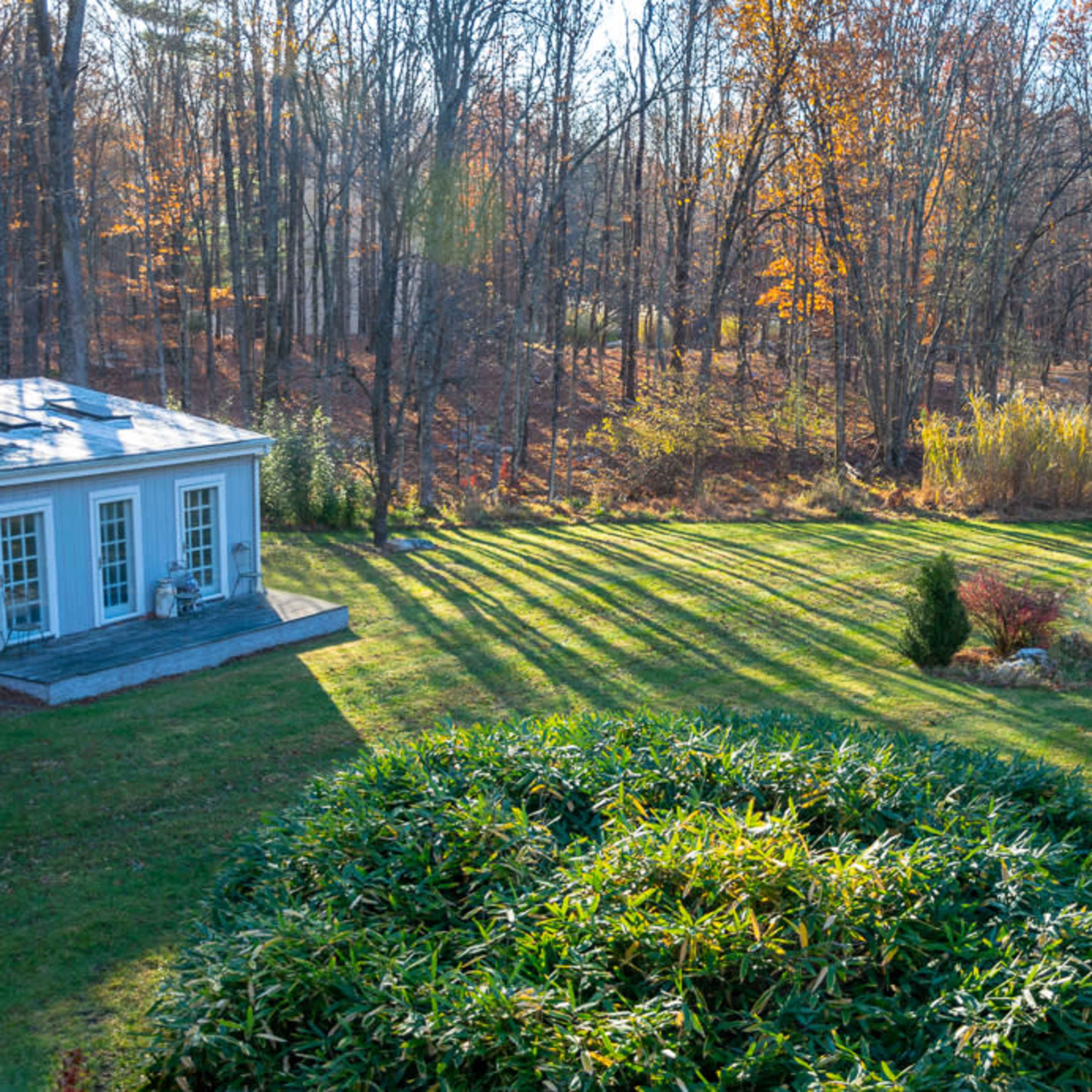 A landscaped garden with geometric patterns of shadows created by trees and a nearby building, set in a natural wooded area.