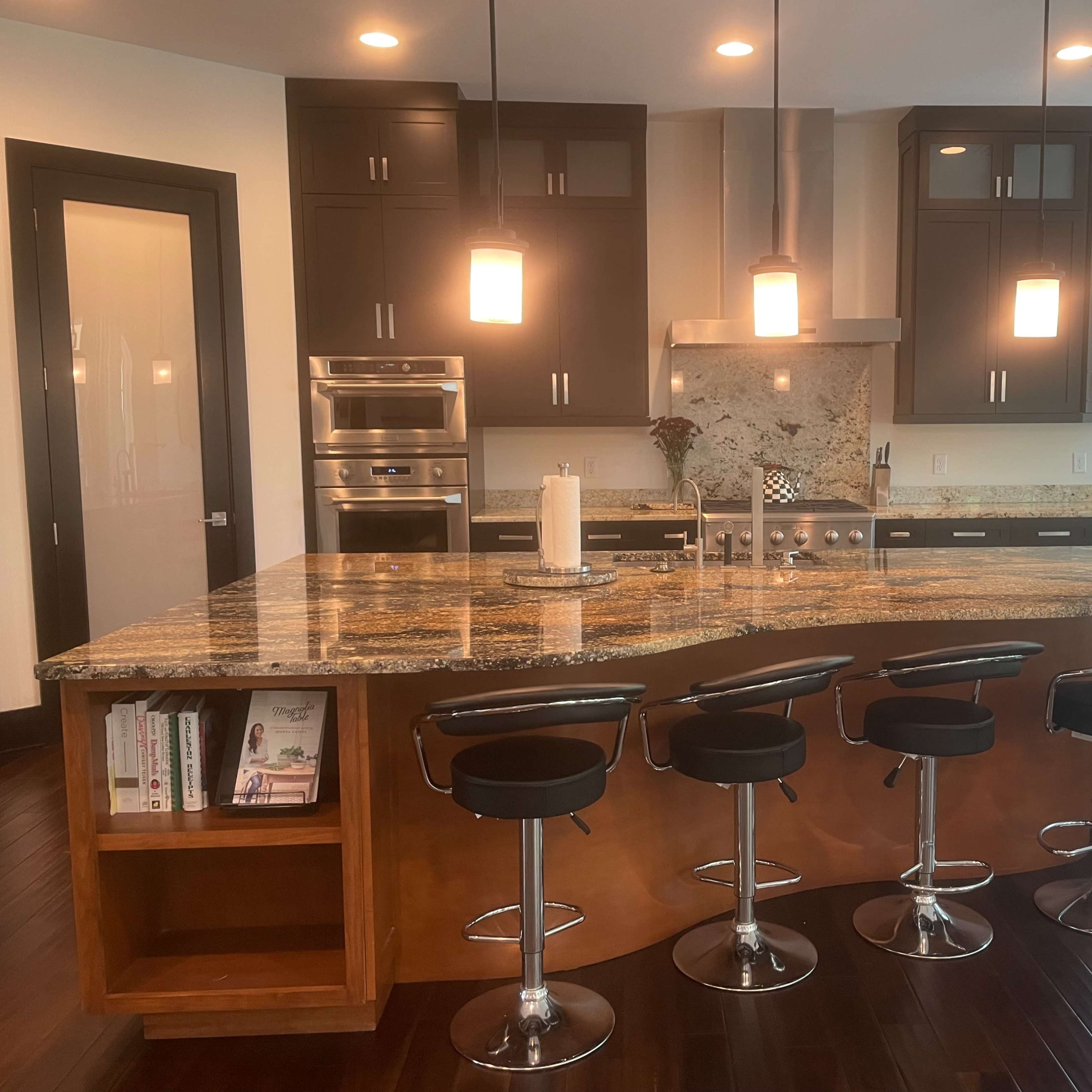 A modern kitchen featuring dark cabinetry, a large granite island with bar stools, and stainless steel appliances.