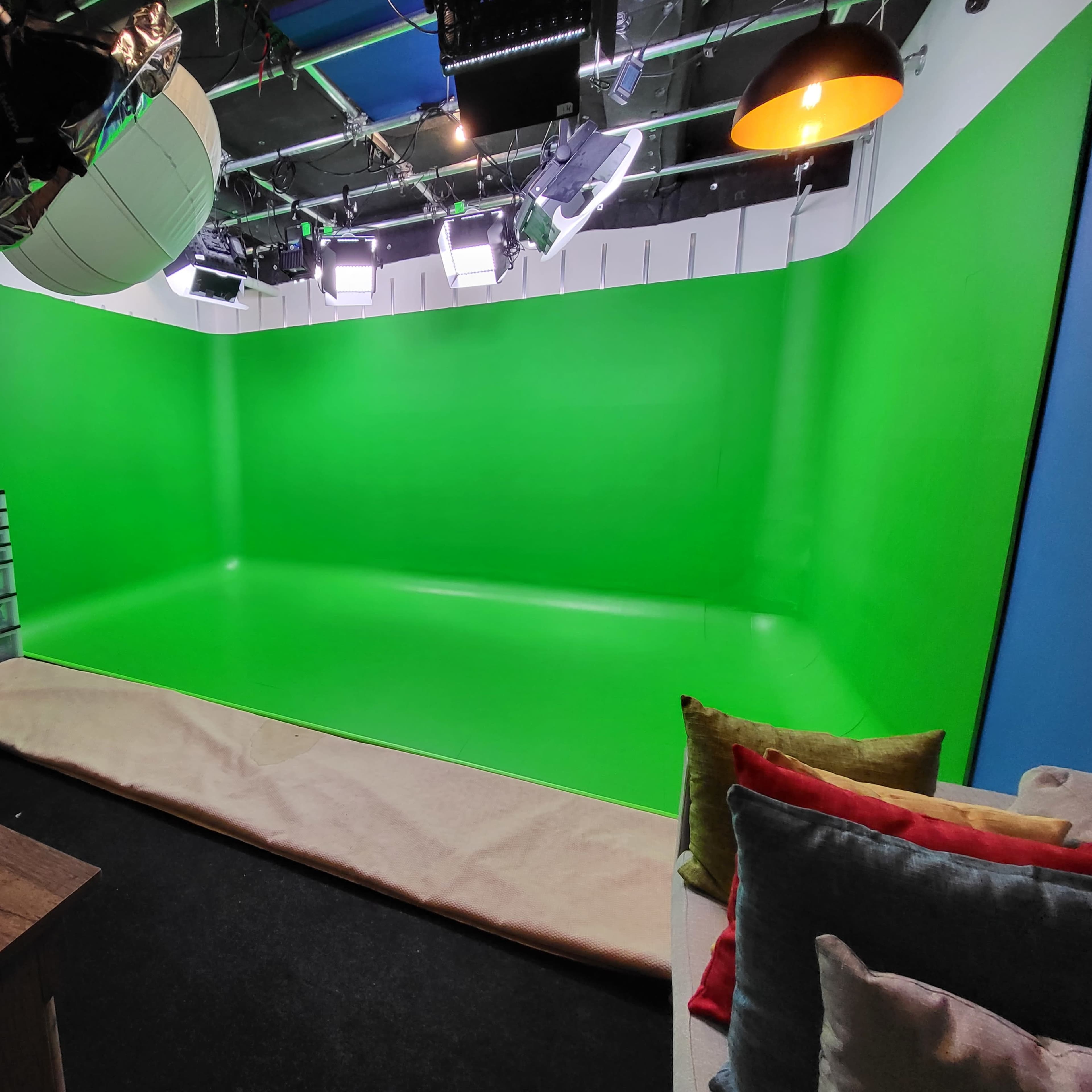A green screen studio setup with bright lighting, a wooden table, and a sofa with cushions in the foreground.