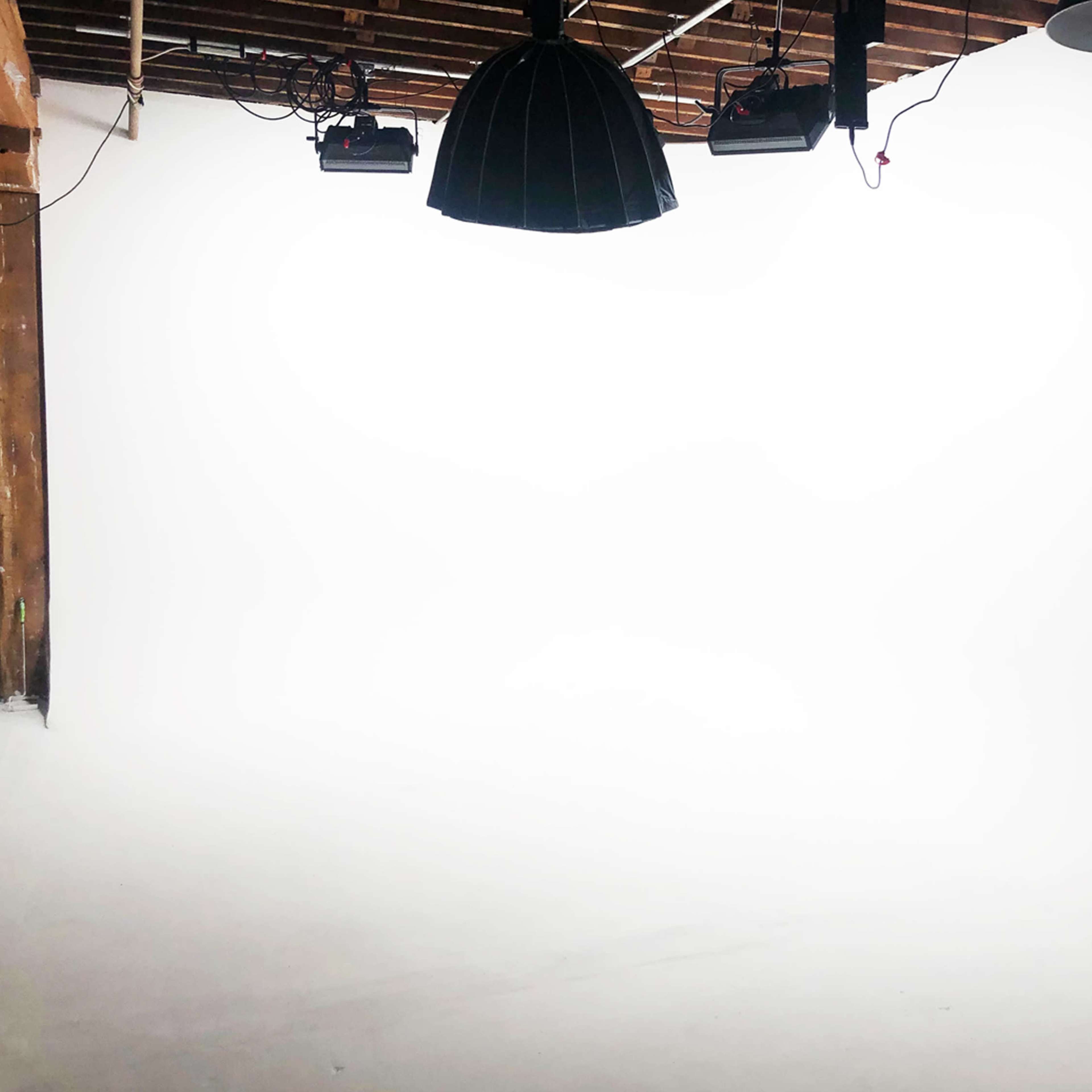 A spacious photography studio features a white backdrop, overhead lights, and exposed wooden beams.
