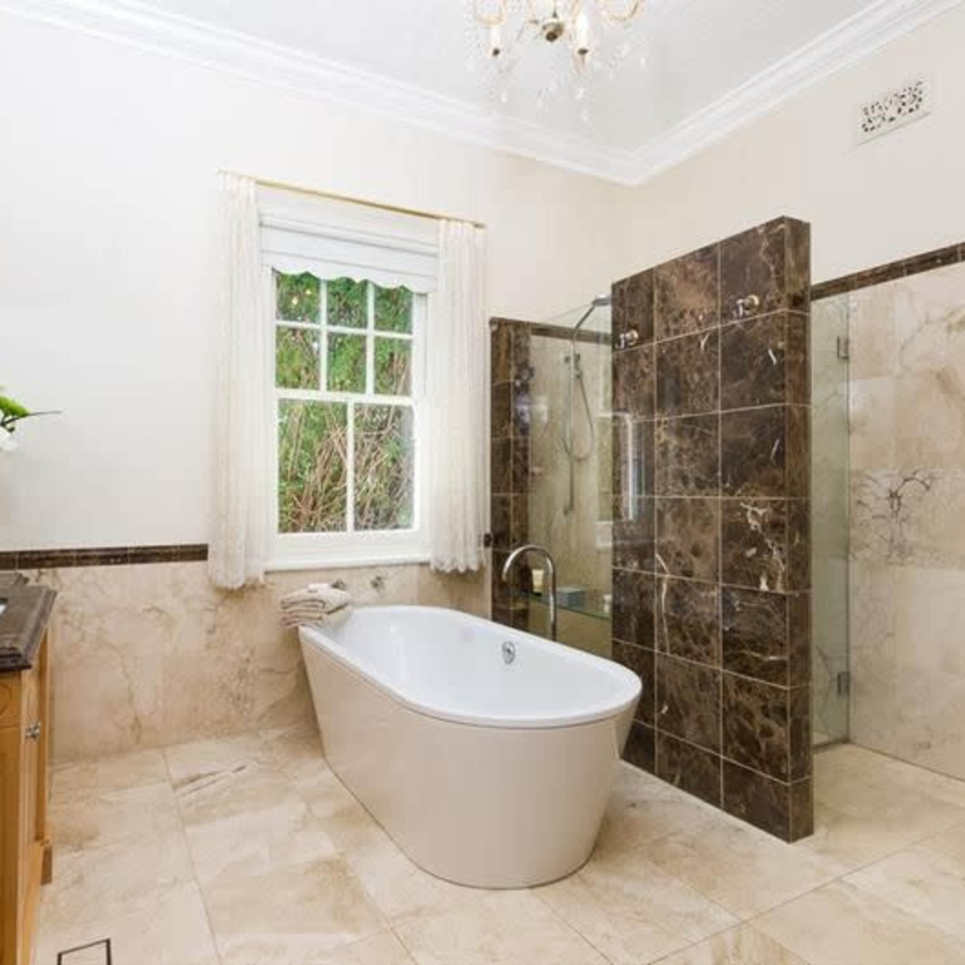 The bathroom features a freestanding tub, a glass shower enclosure, and marble walls with a wooden vanity.