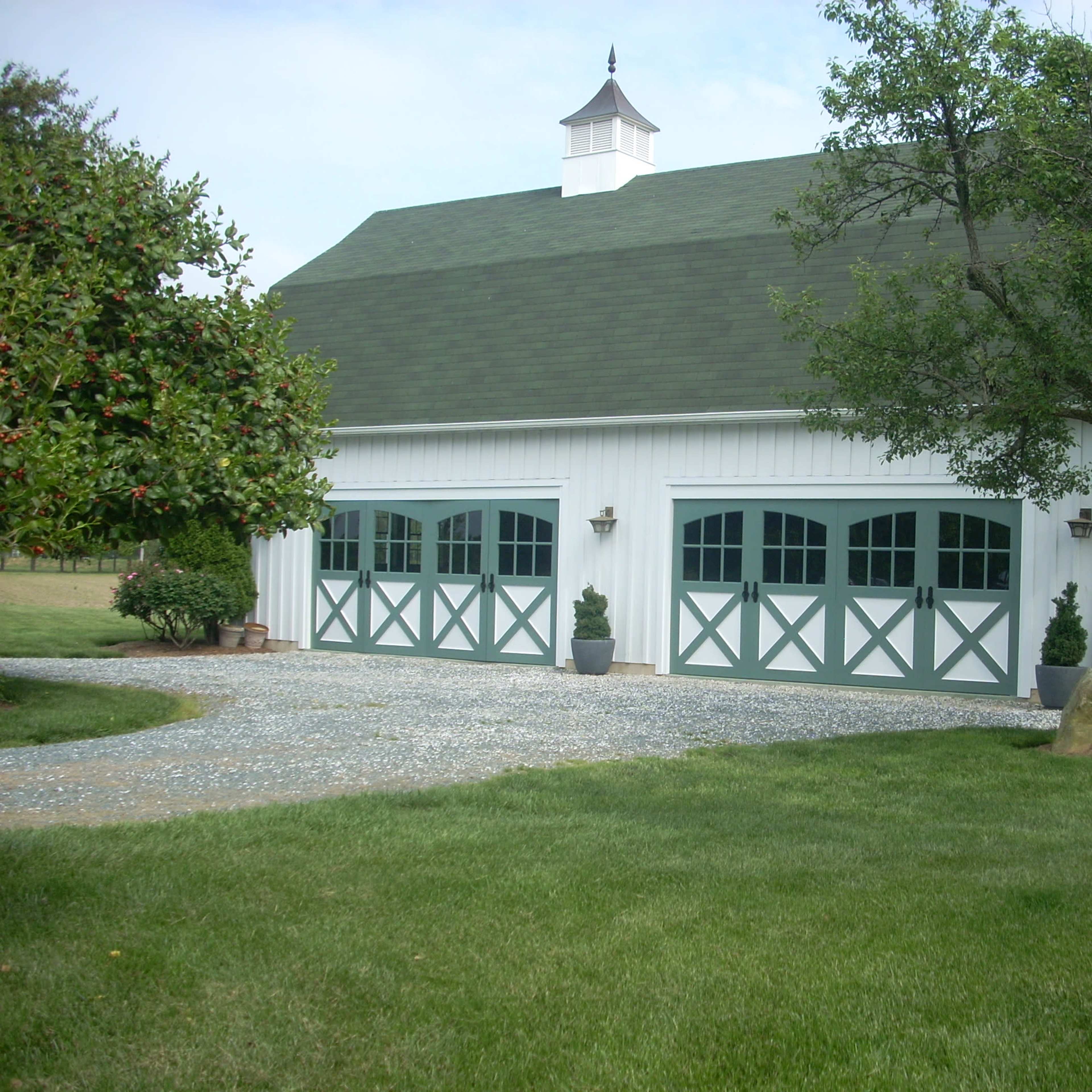 A white barn-style building with green accents, featuring large garage doors and a landscaped yard.