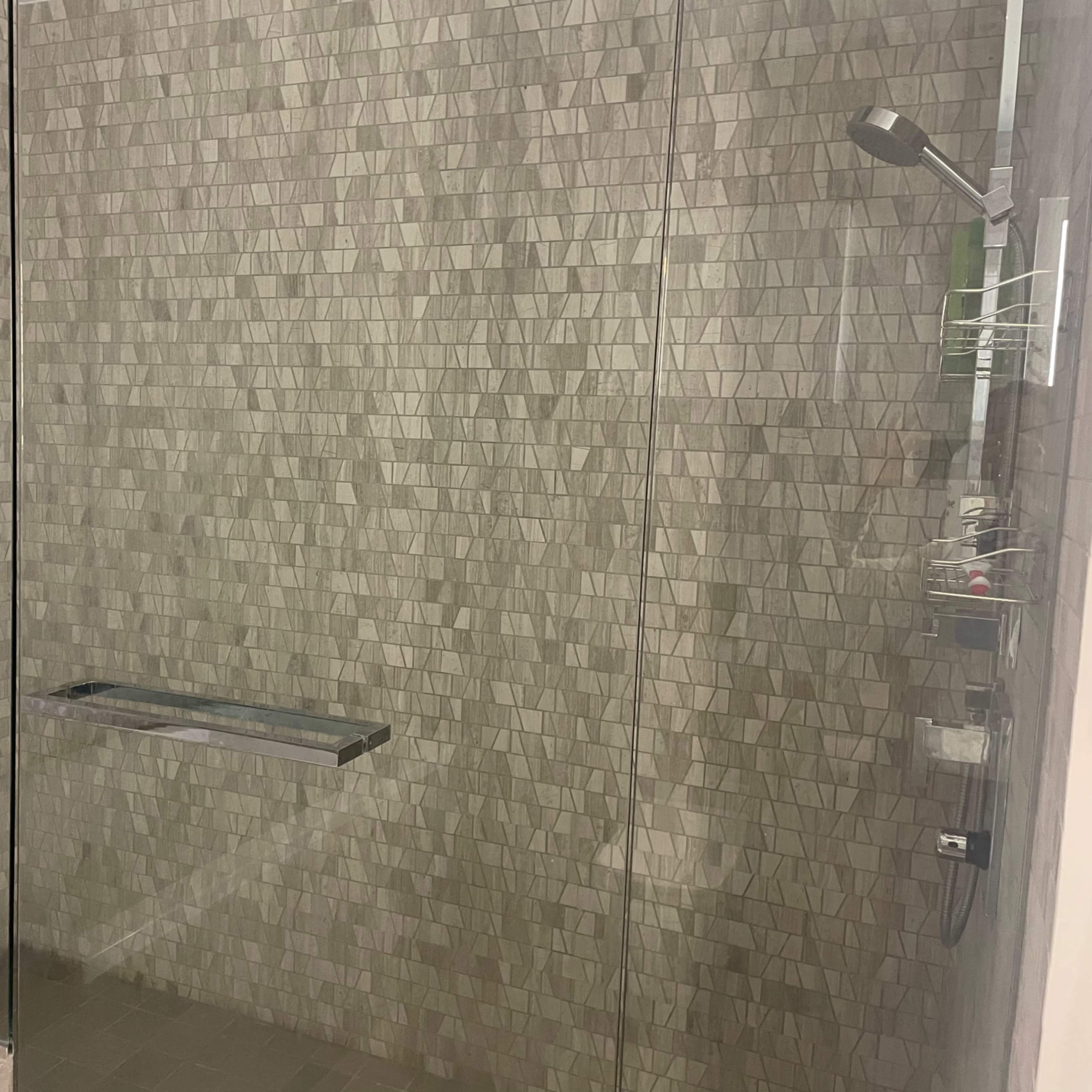 A modern shower with a glass enclosure featuring tiled walls and a showerhead mounted on one side.