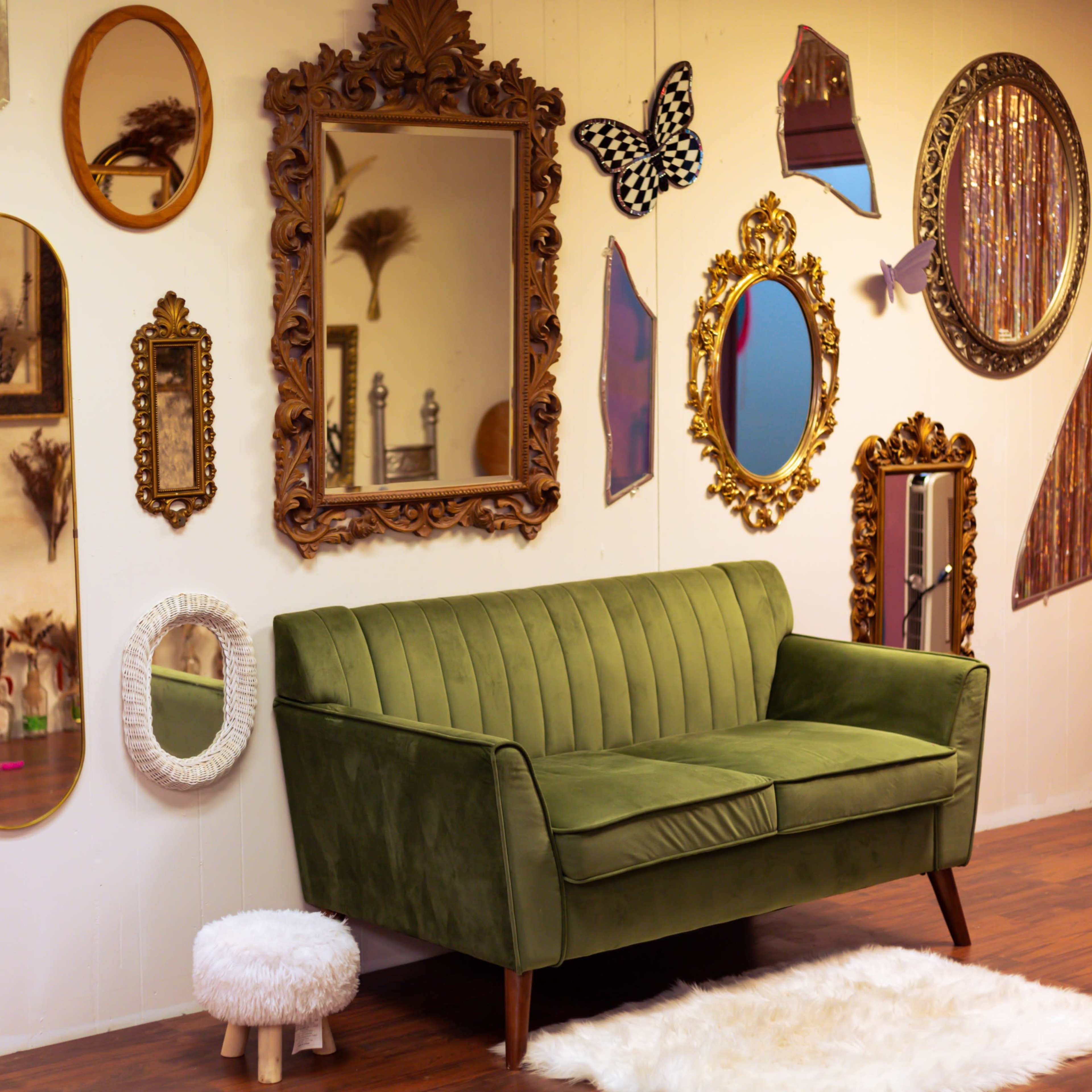 A green velvet couch positioned next to a wall adorned with various mirrors, frames, and decorative objects.