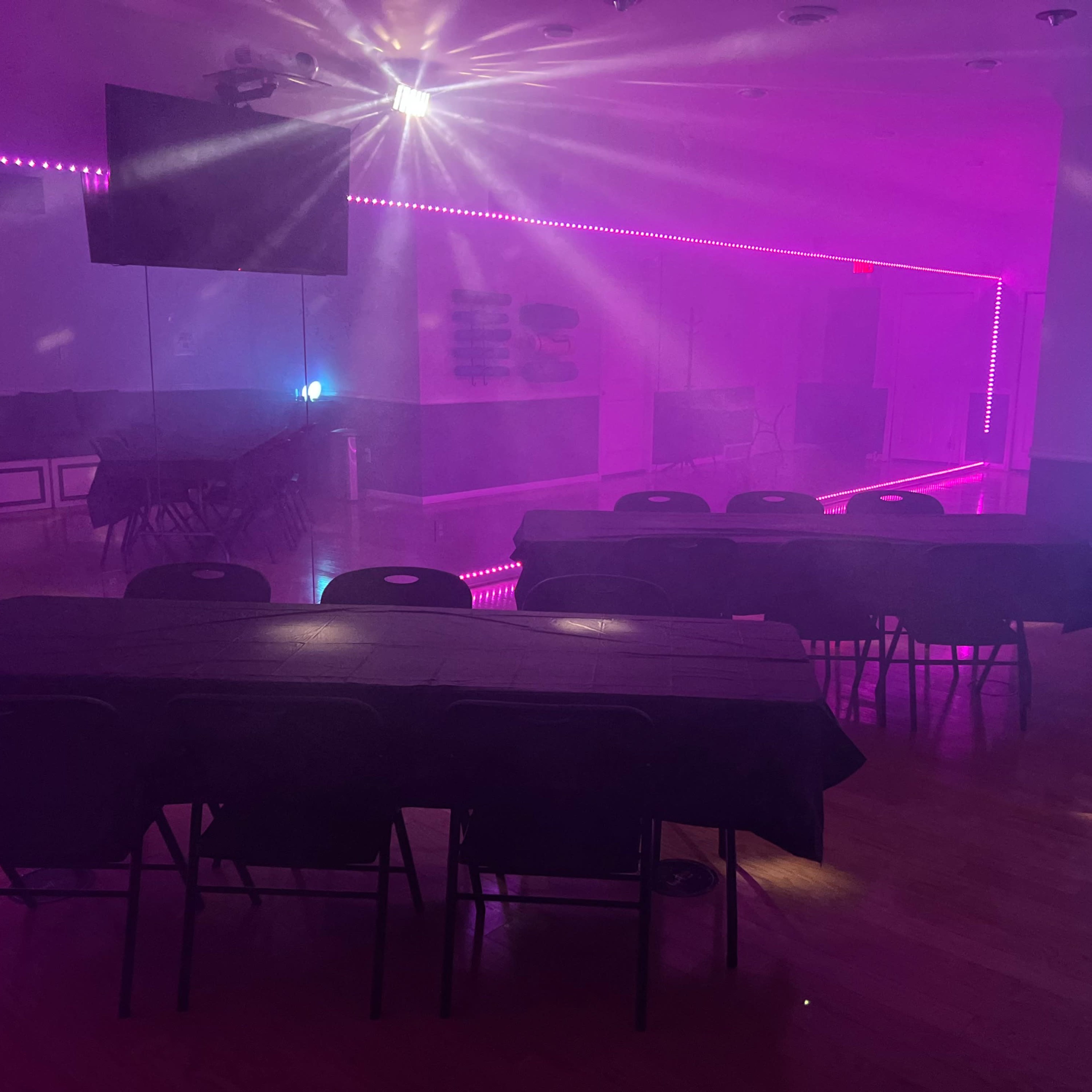 A dimly lit room with several black tables and purple lighting along the walls.