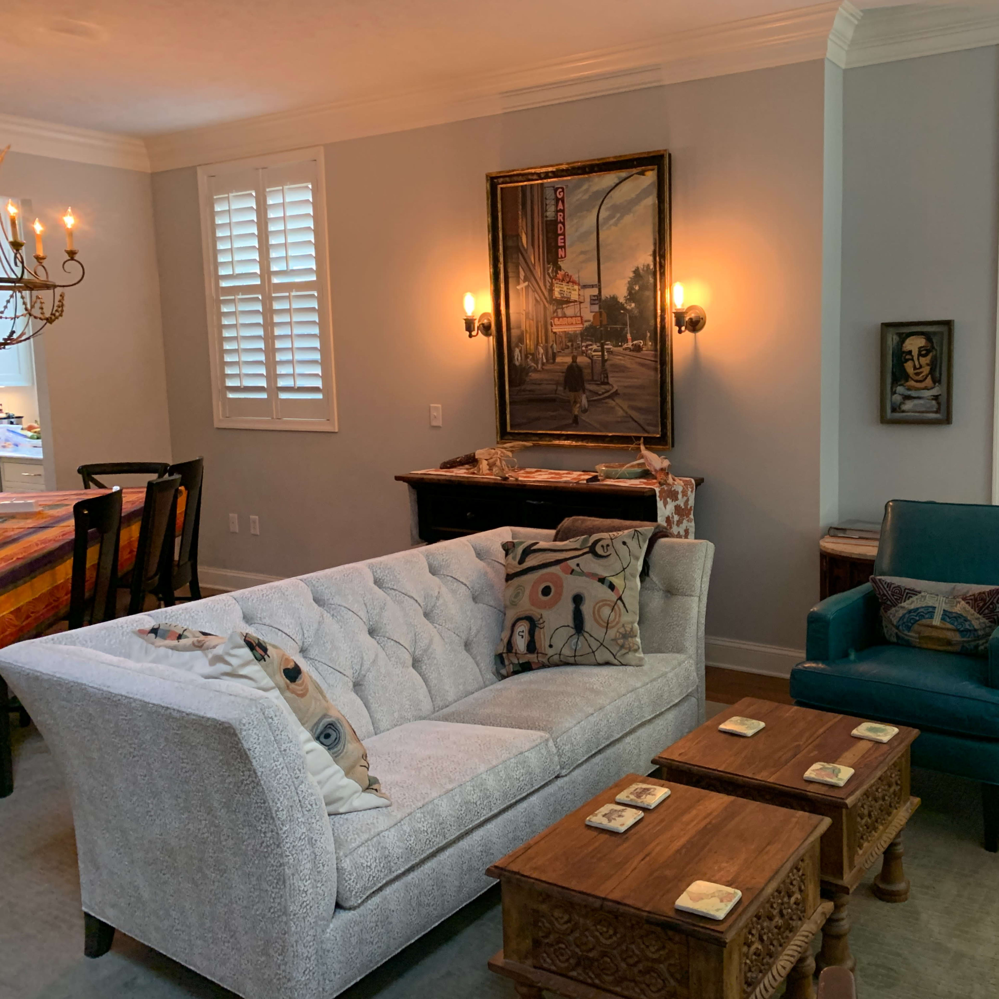 A living room with a gray tufted sofa, two teal armchairs, wooden coffee tables, and artwork on the walls.