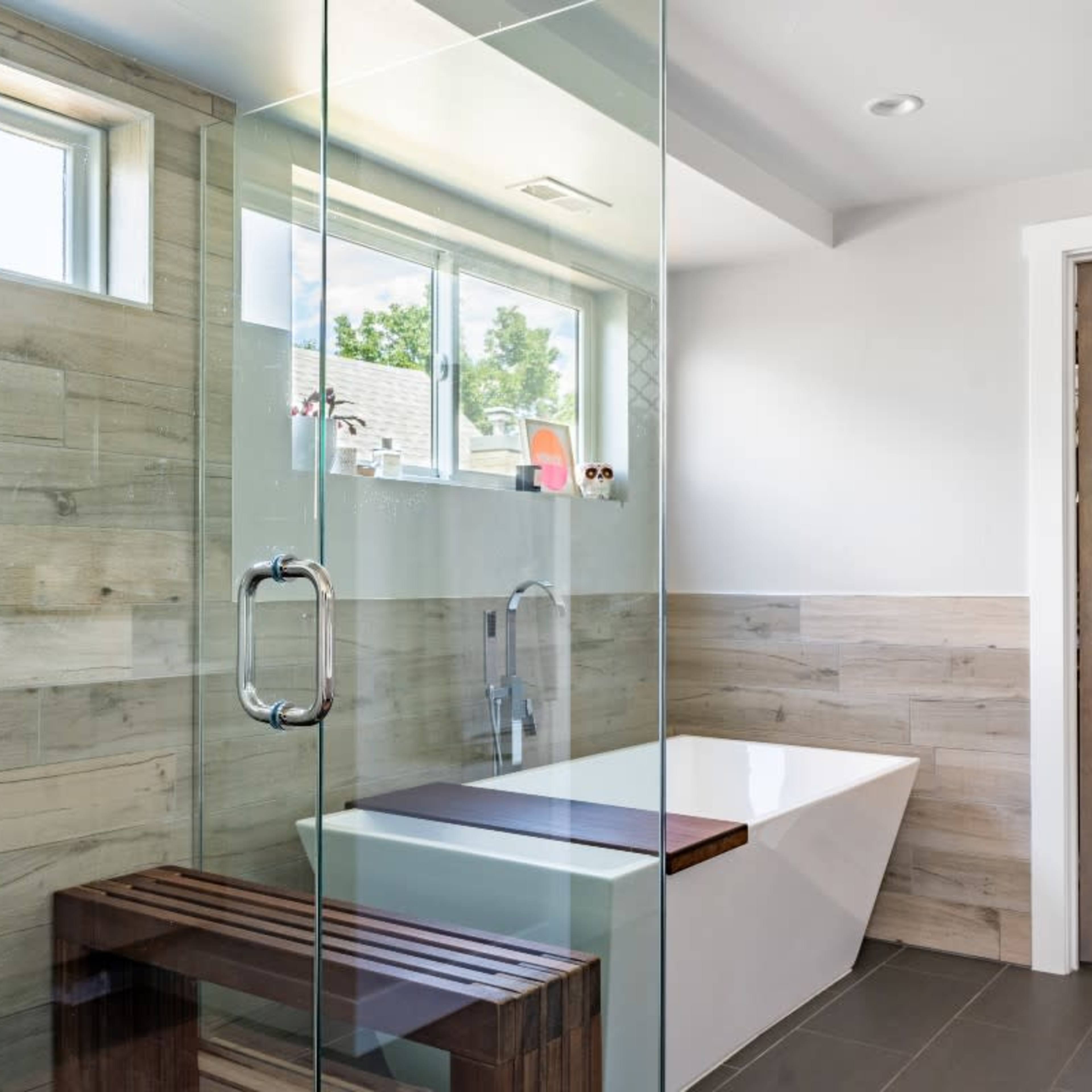 A modern bathroom featuring a glass shower enclosure, a freestanding bathtub, and wood-paneled walls.