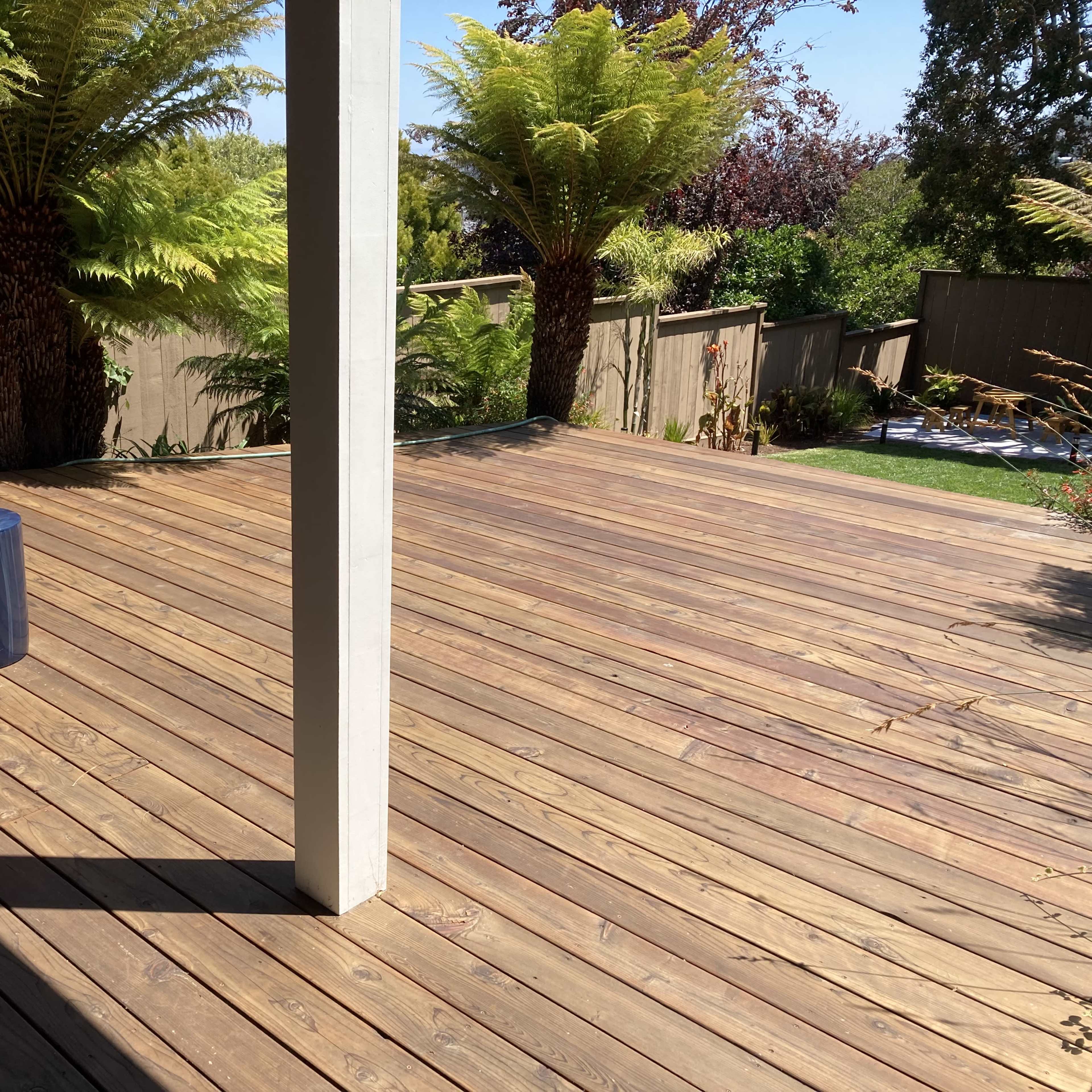 A wooden deck with orange chairs, a small blue table, and lush green plants in the background.