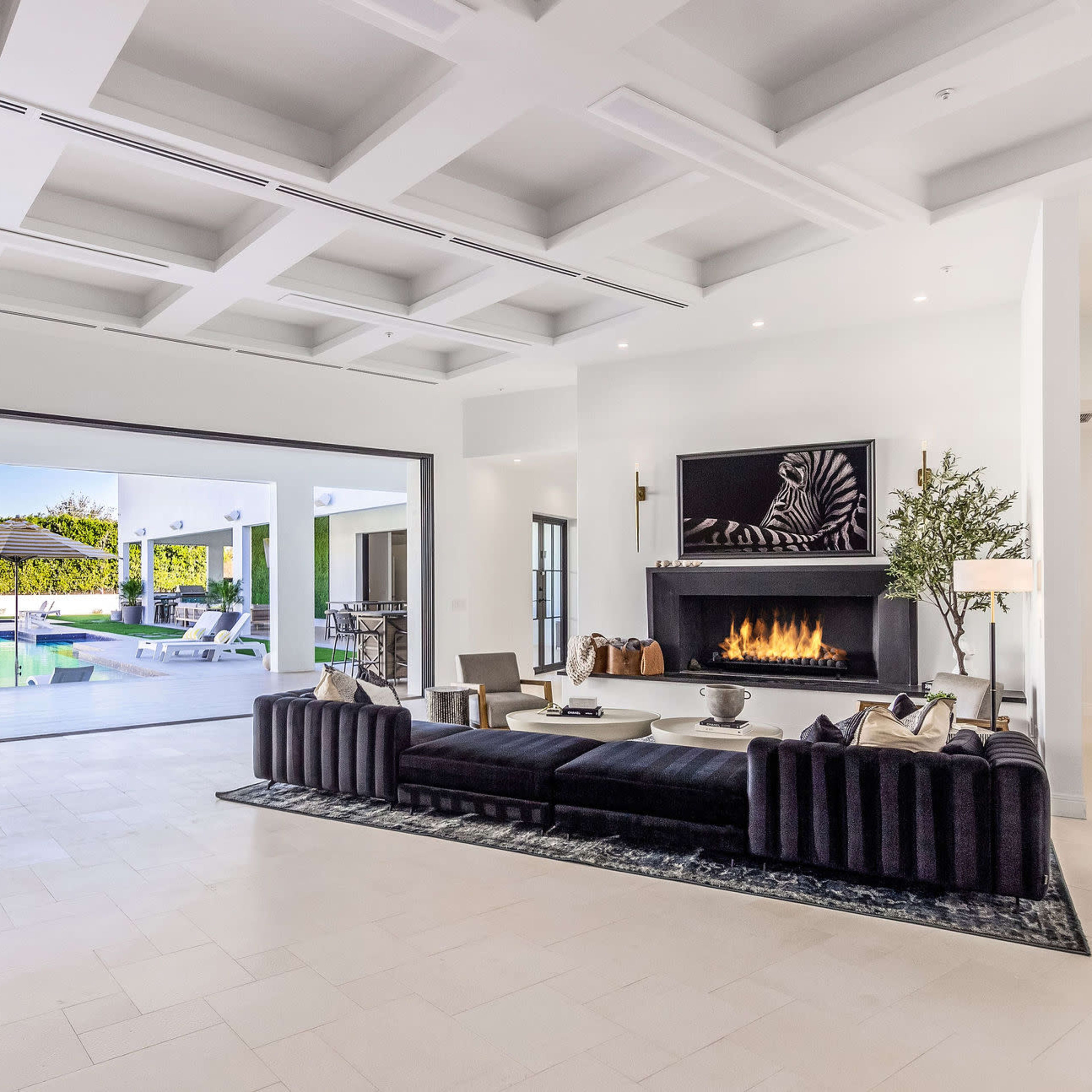 A modern living room with a large sectional sofa and a fireplace, leading to an outdoor pool area through expansive sliding glass doors.