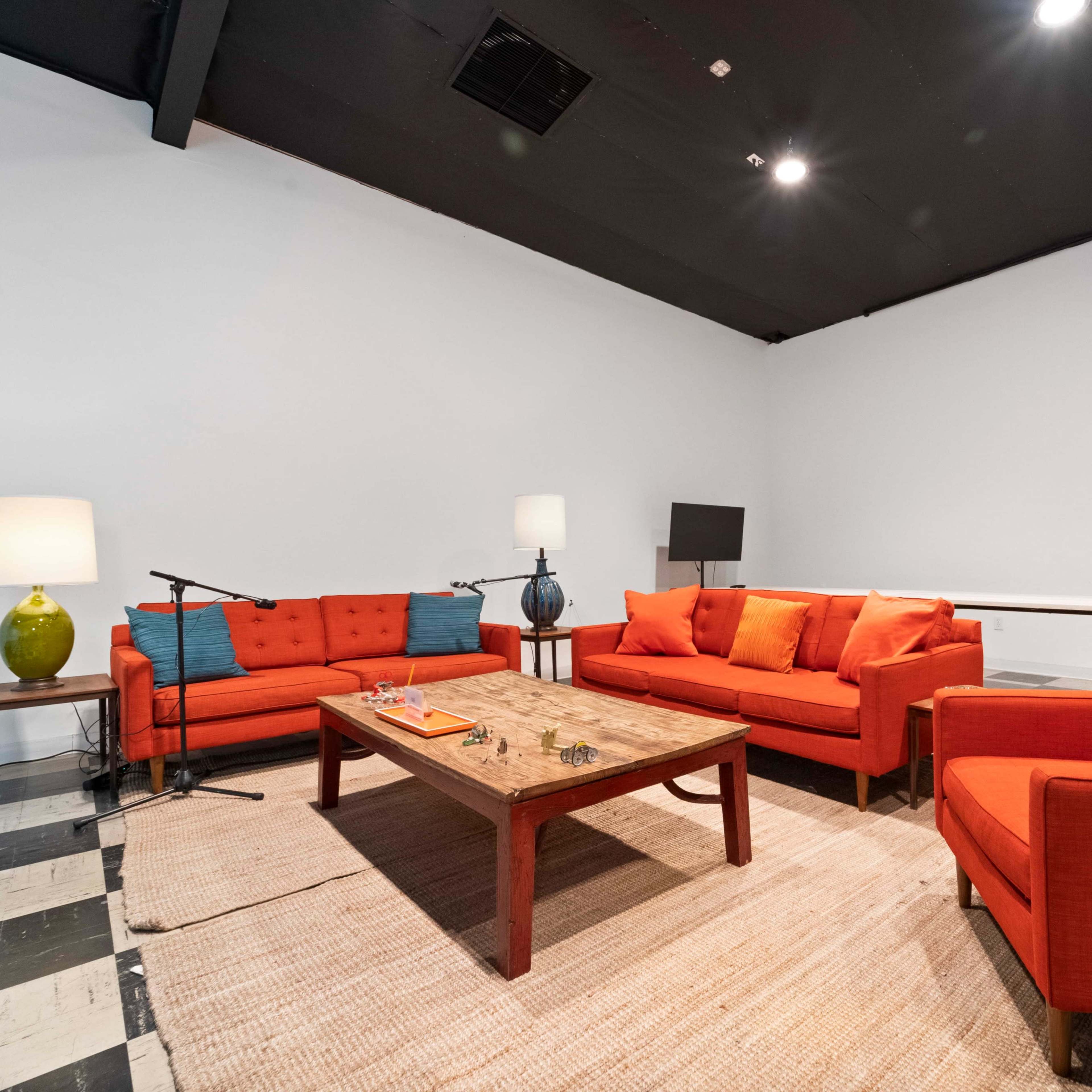 The scene features a contemporary seating area with orange sofas arranged around a wooden coffee table on a light-colored rug.
