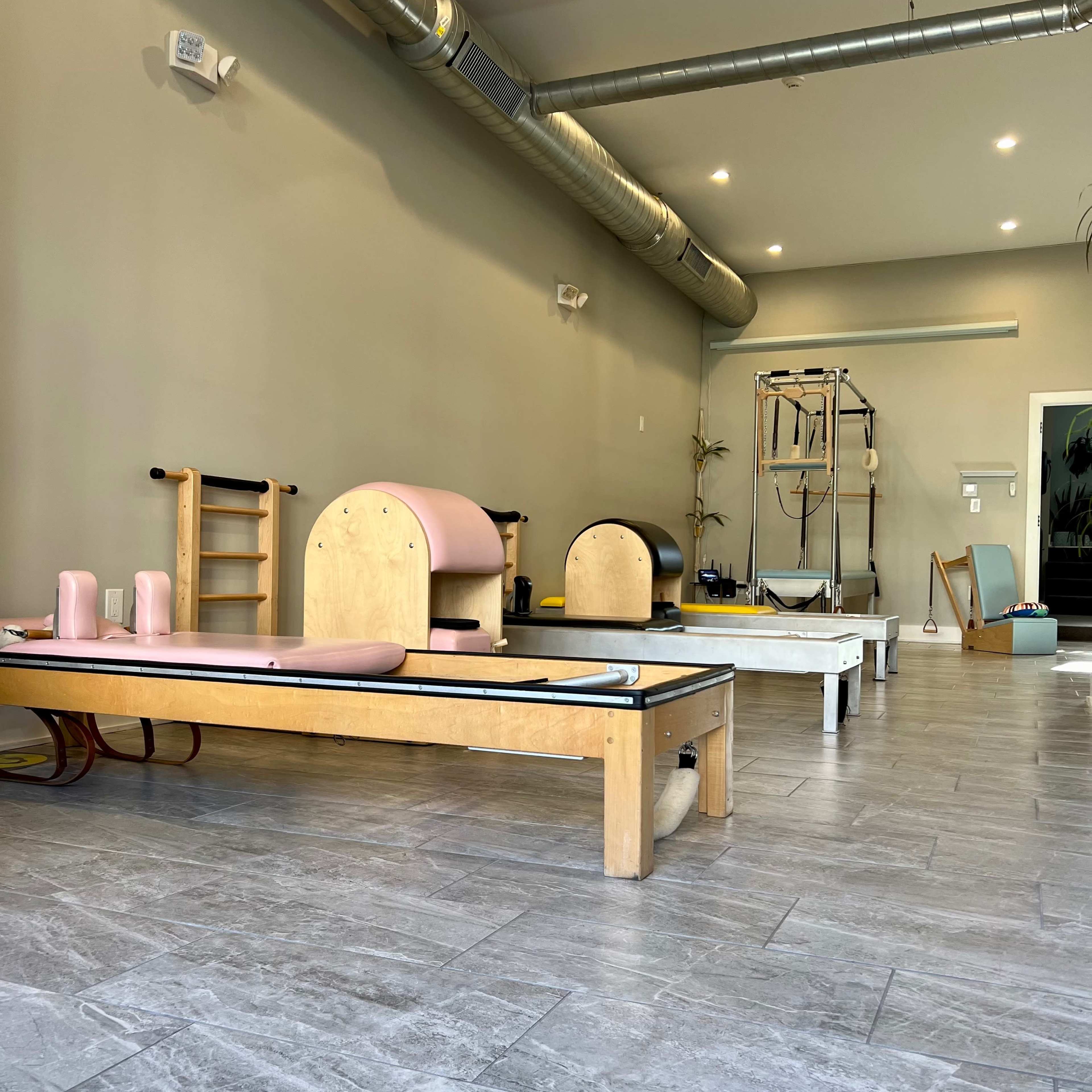 A spacious Pilates studio with wooden reformers and equipment arranged neatly on gray tiled flooring.