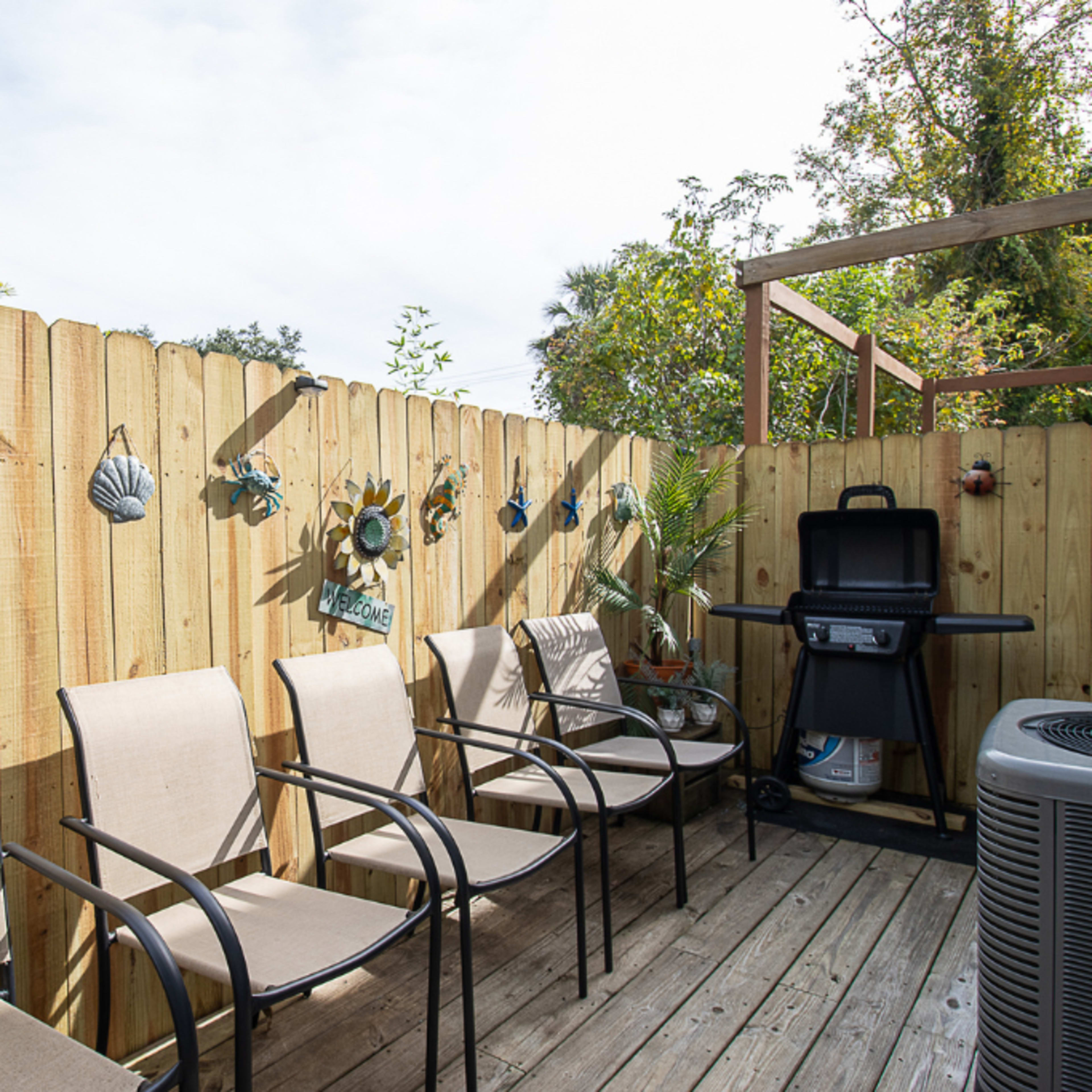 A wooden deck with four metal-framed chairs, a grill, and various sea-themed decorations mounted on a wooden fence.
