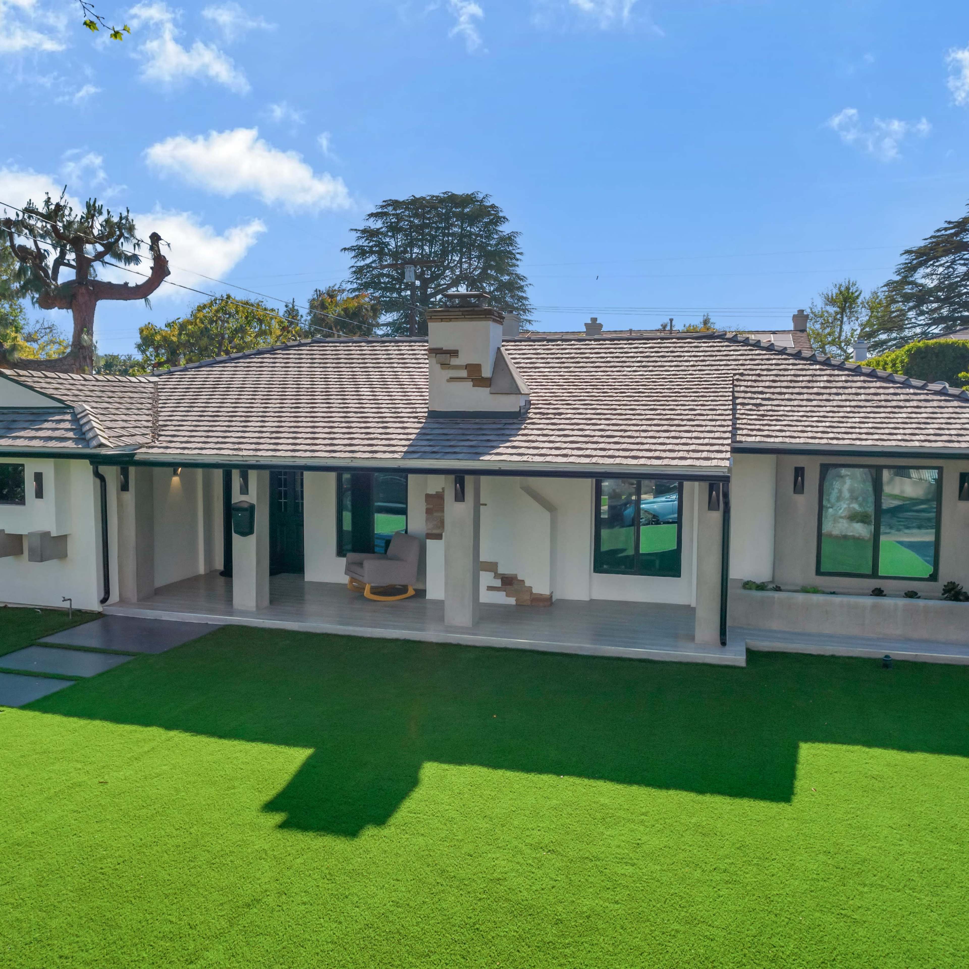 A modern single-story house with a sloped roof is set on a landscaped yard featuring artificial grass and stone pathway.
