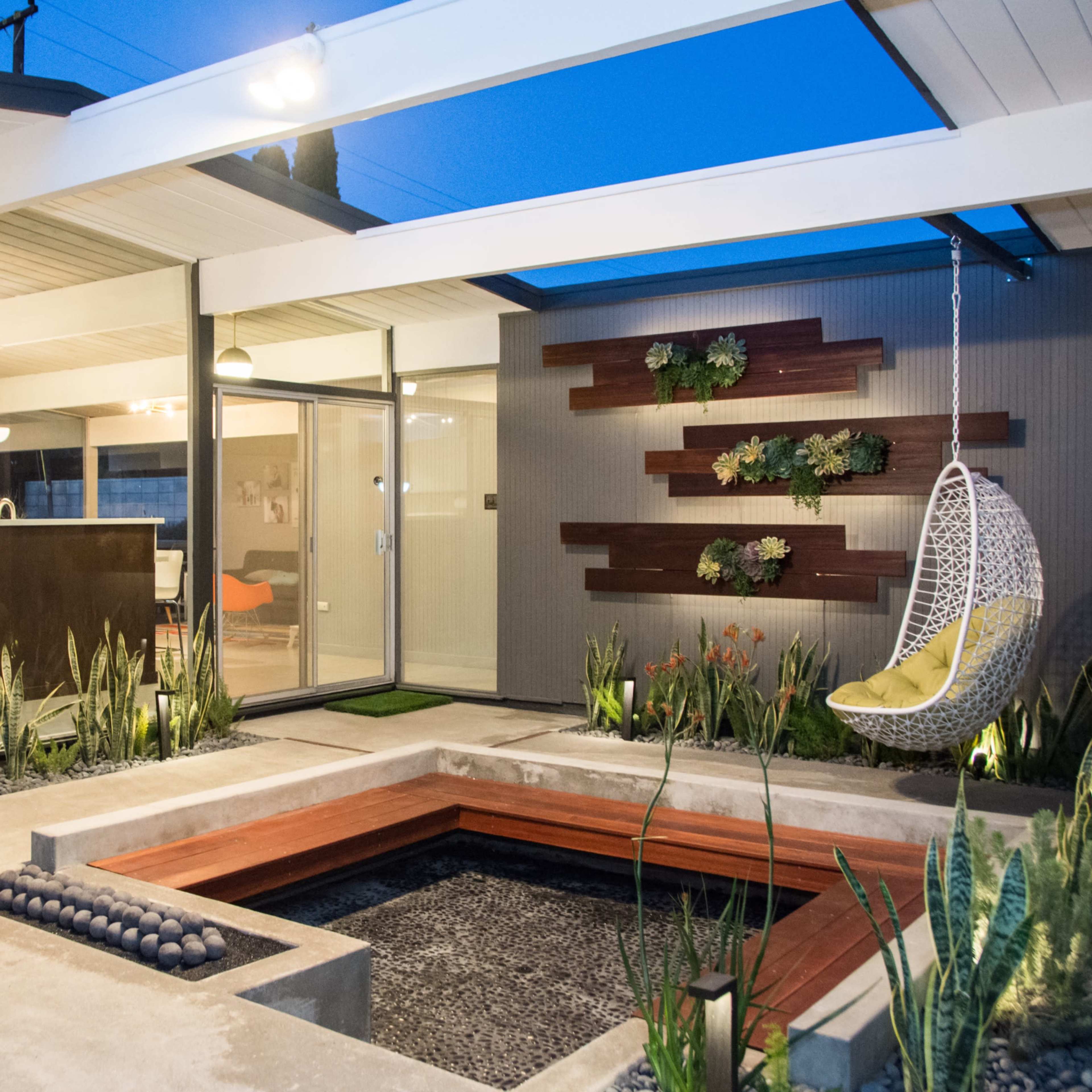 A modern courtyard featuring a gel-filled central planter, a hanging chair, and decorative plants against a sleek architectural backdrop.