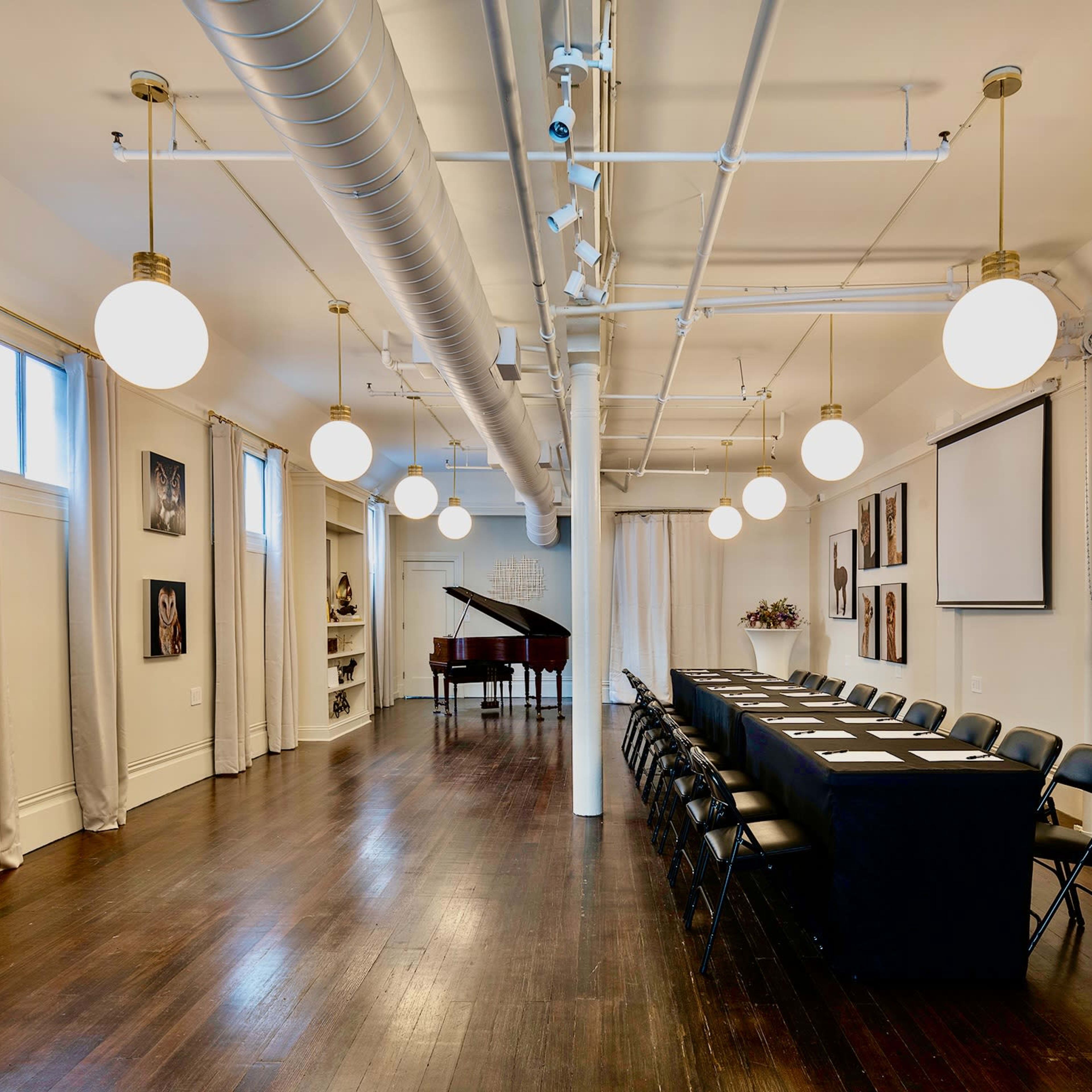 A large, well-lit conference room features a long table with chairs, a grand piano in the corner, and framed photographs on the walls.