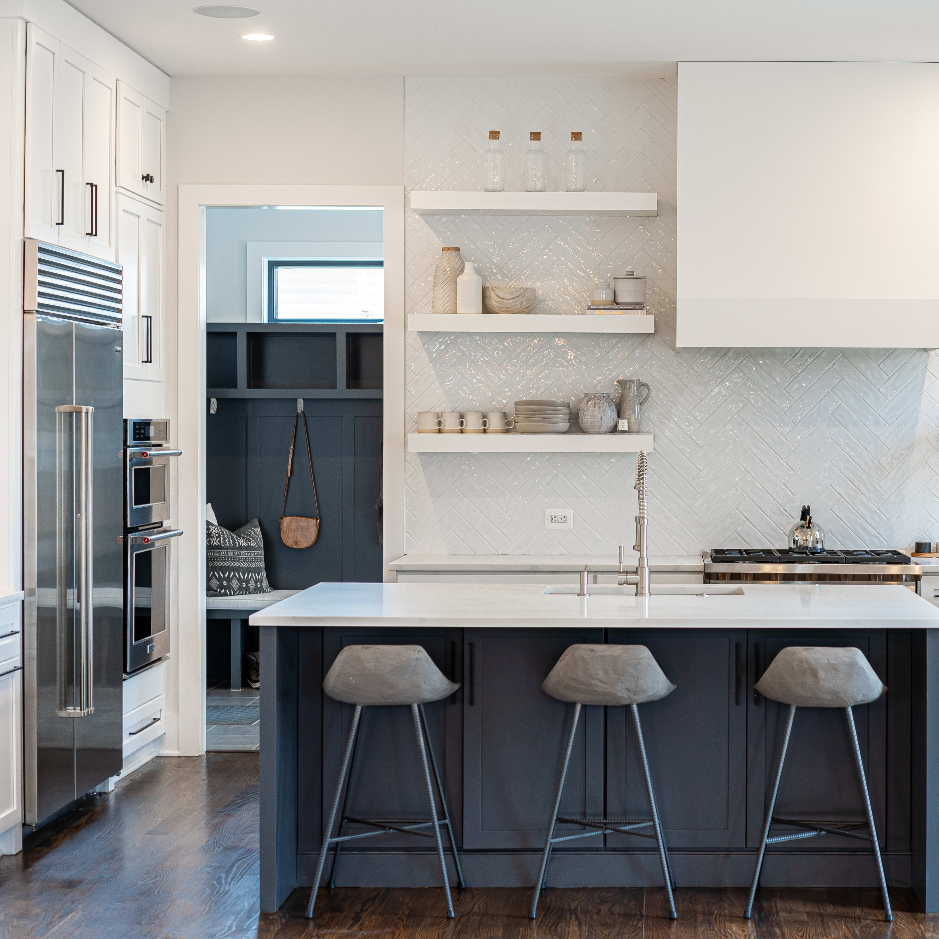 A modern kitchen features a large island with three stools, white cabinetry, open shelving, and contrasting dark cabinetry.