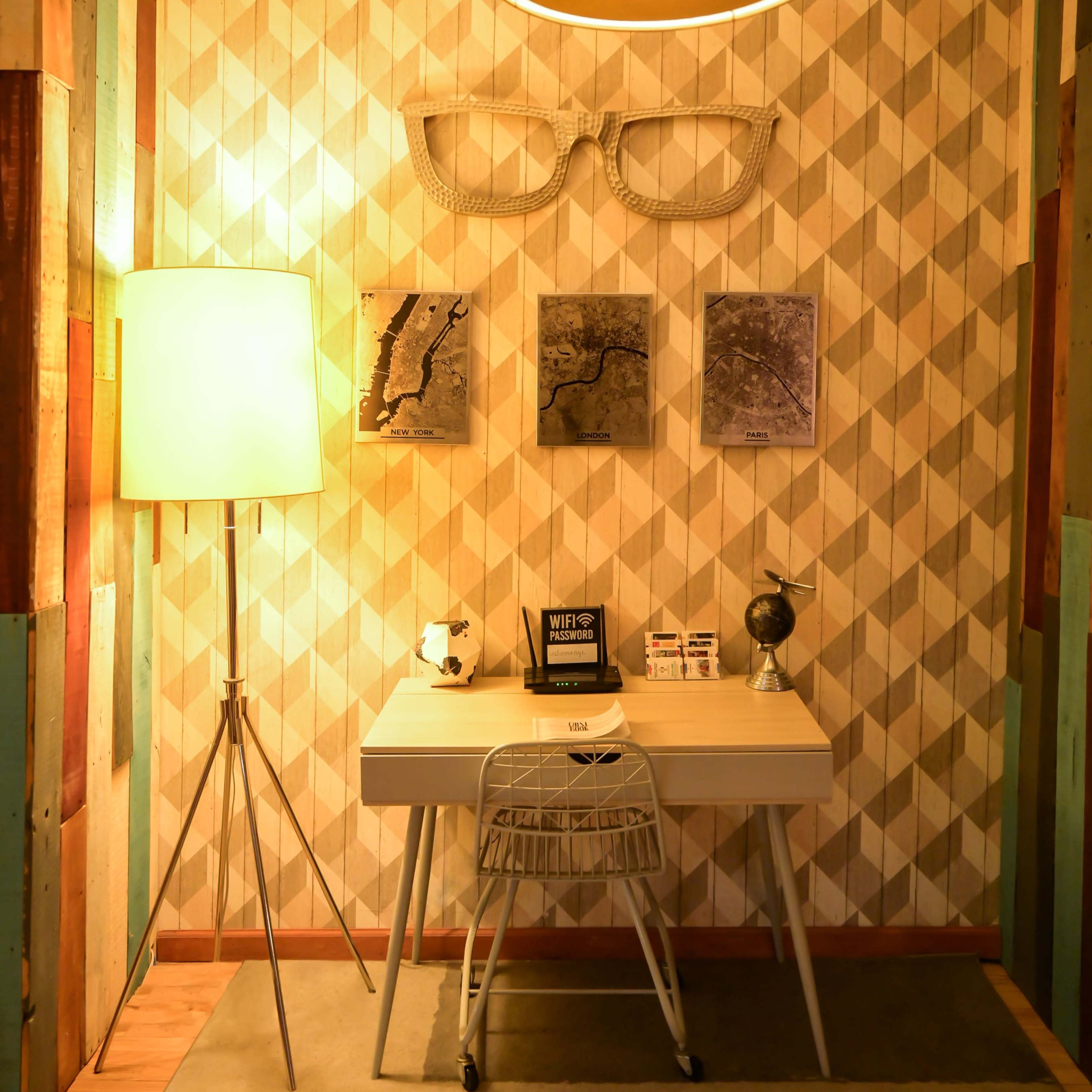 A modern workspace featuring a white desk with a single chair, accompanied by decorative wall art and distinct lighting fixtures.