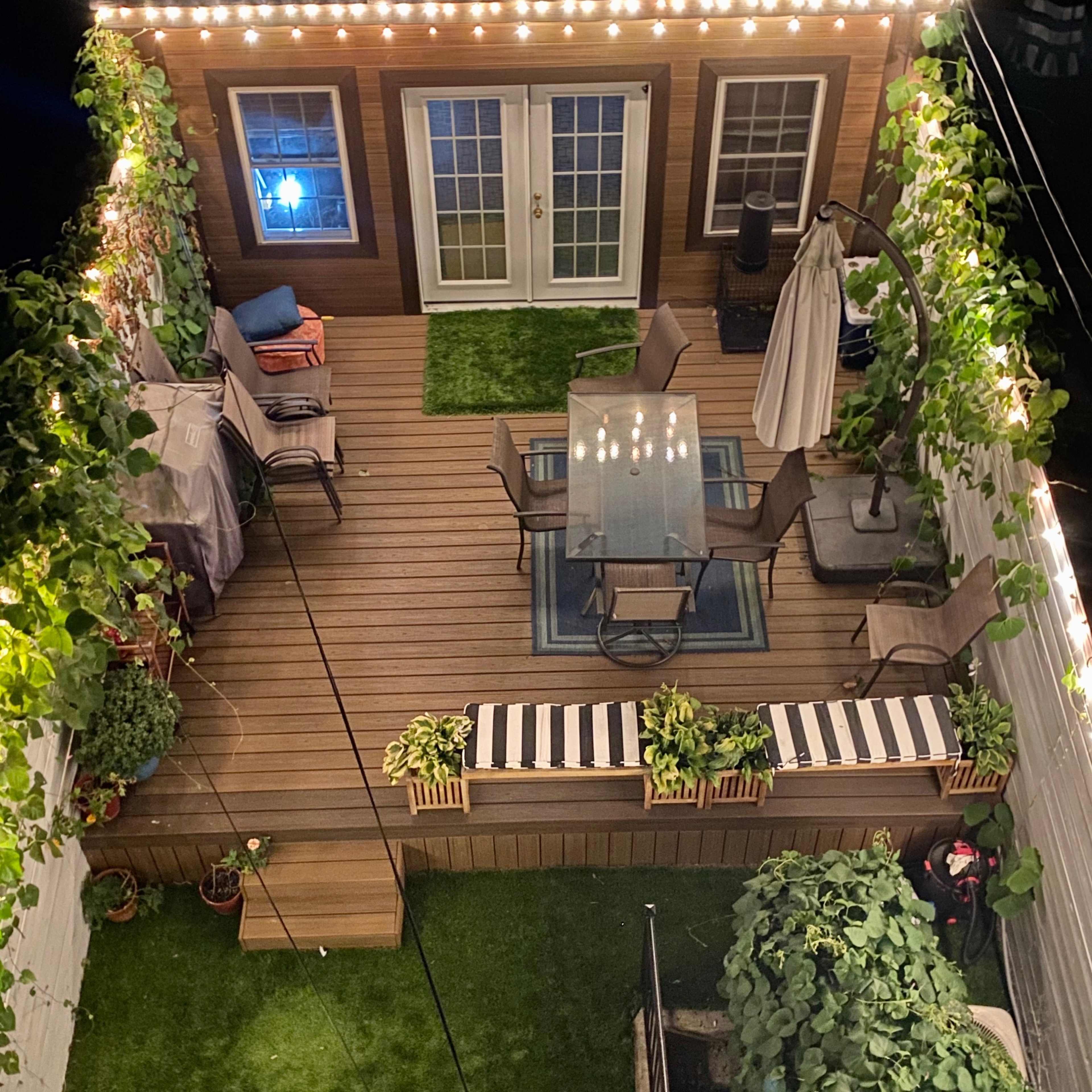 A well-decorated backyard deck featuring a dining table set with chairs, potted plants, and string lights illuminating the area.