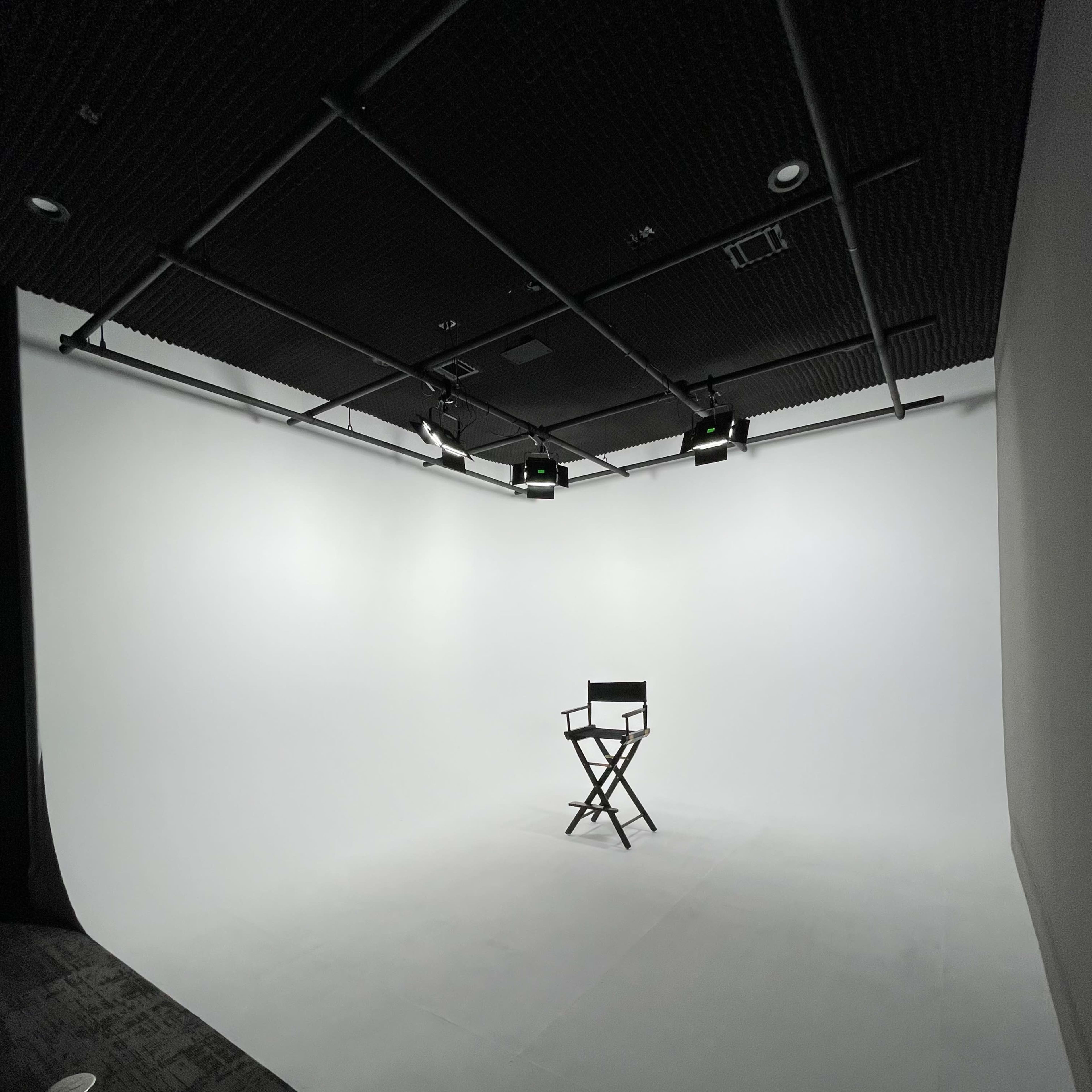 A minimalistic studio space with a single black director's chair against a white backdrop, illuminated by overhead lights.