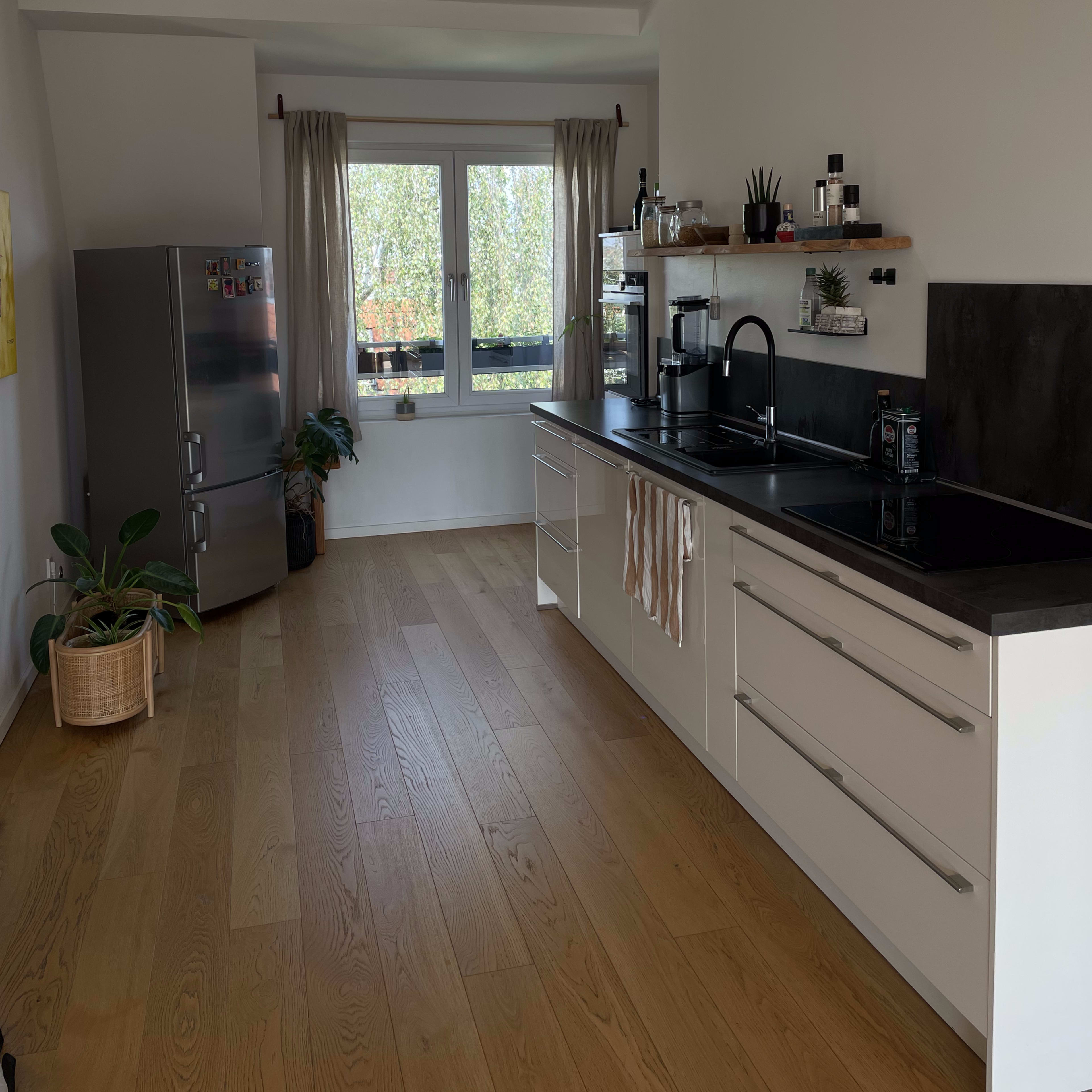 A modern kitchen features sleek cabinetry, a black countertop, and large windows with natural light filling the space.
