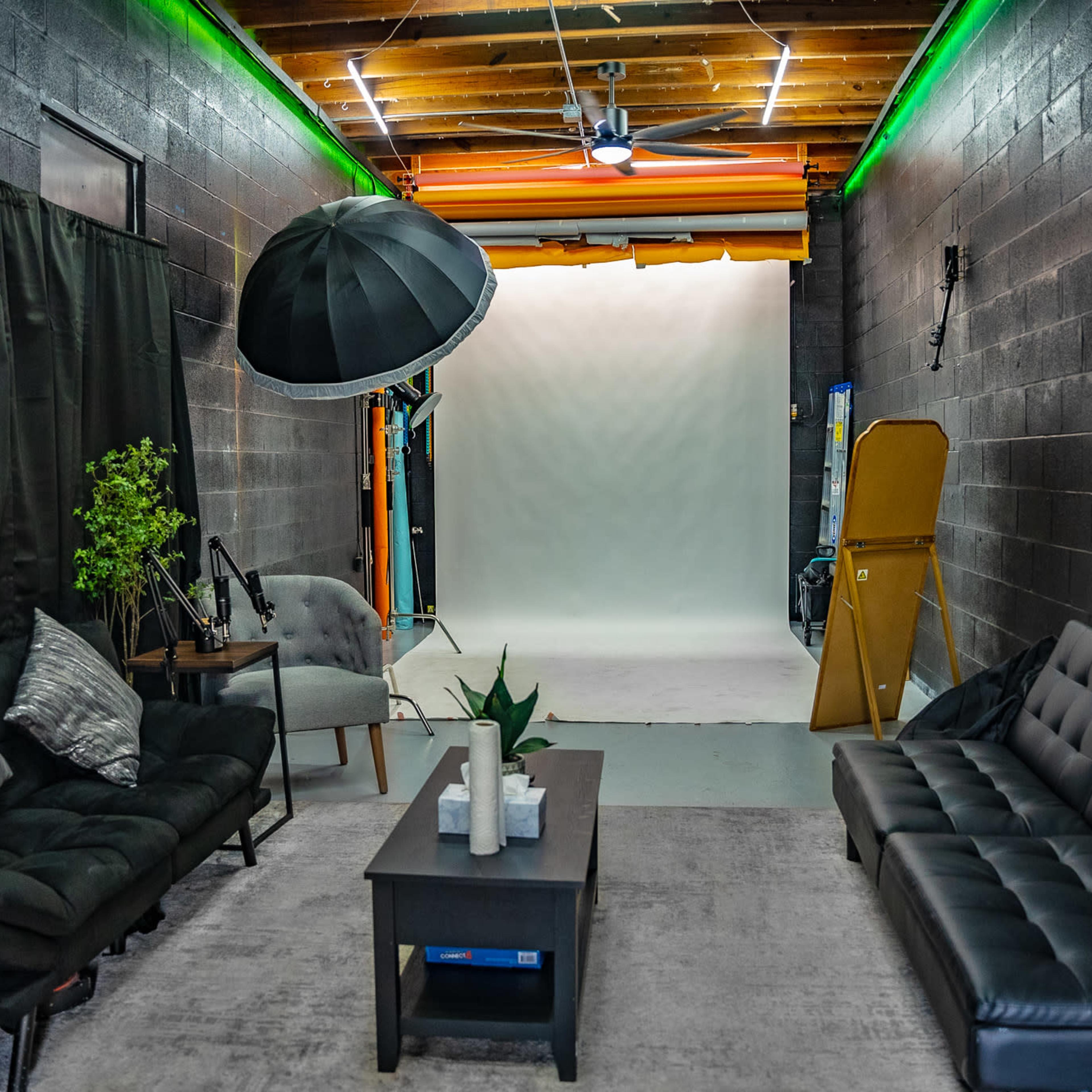 A photography studio featuring a neutral backdrop, seating area with two couches, and equipment including a large umbrella light.