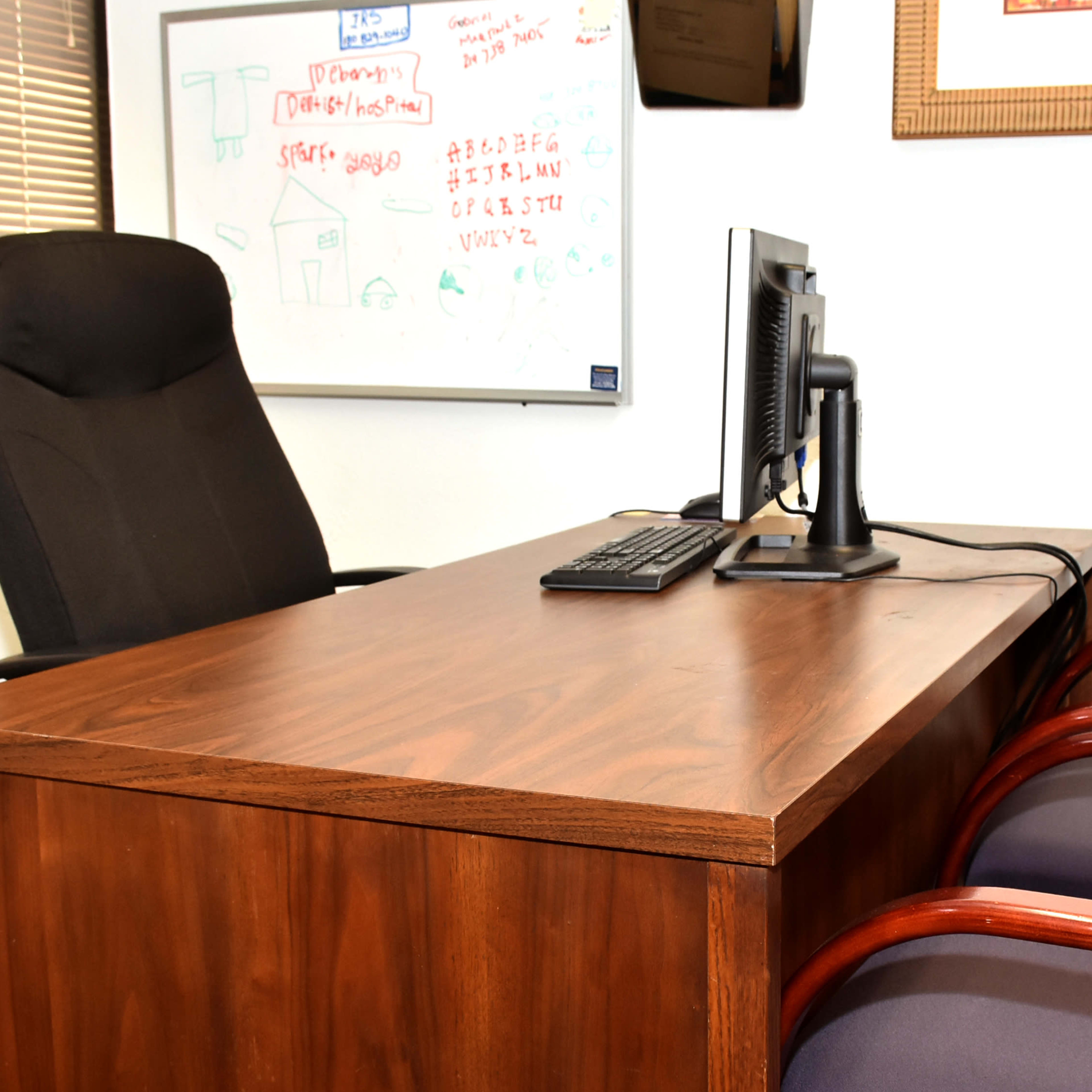 A wooden desk with a computer and keyboard, flanked by two upholstered chairs in an office setting.