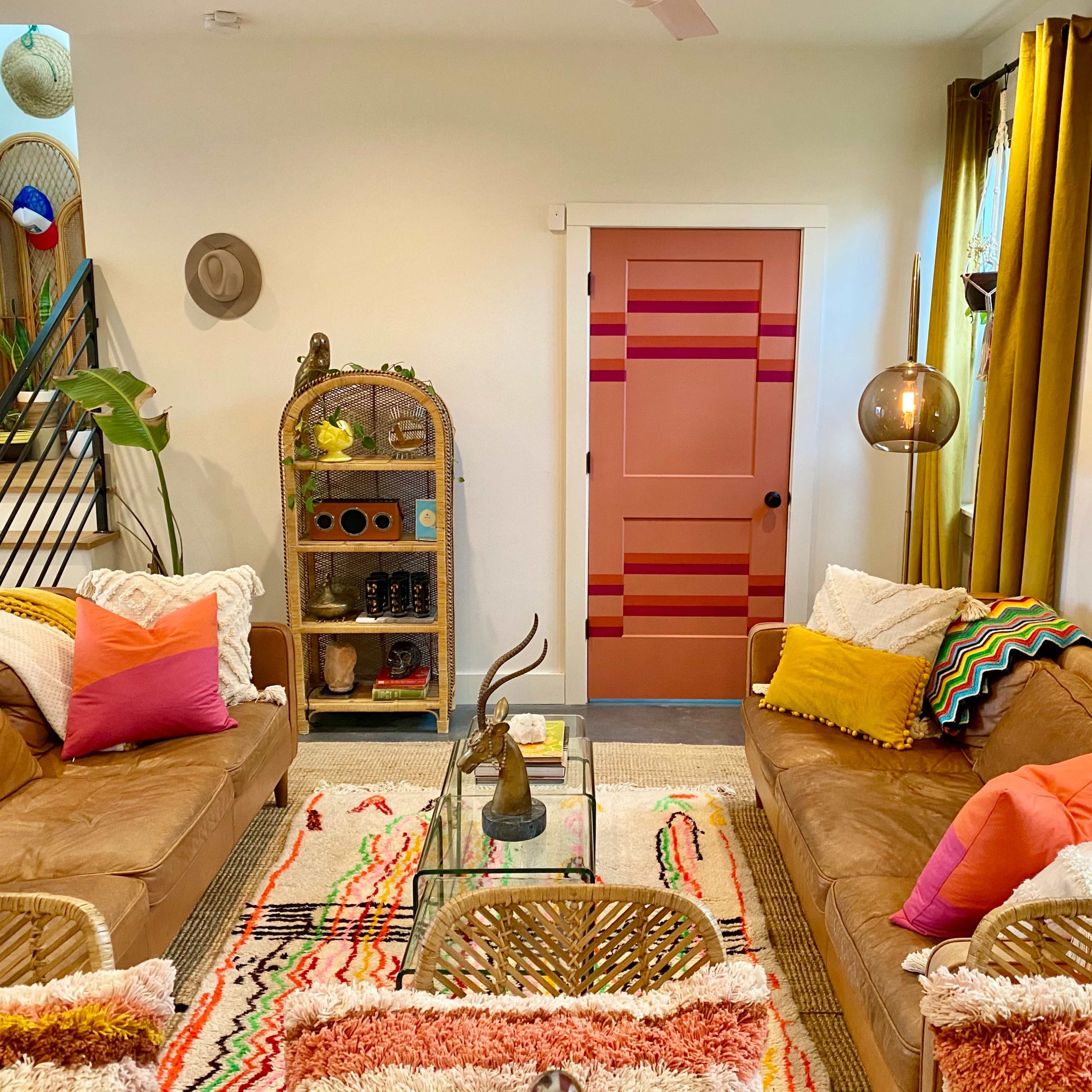 A colorful living room with two brown sofas, a glass coffee table, vibrant throw pillows, a patterned rug, and a decorative wall featuring a door and art.