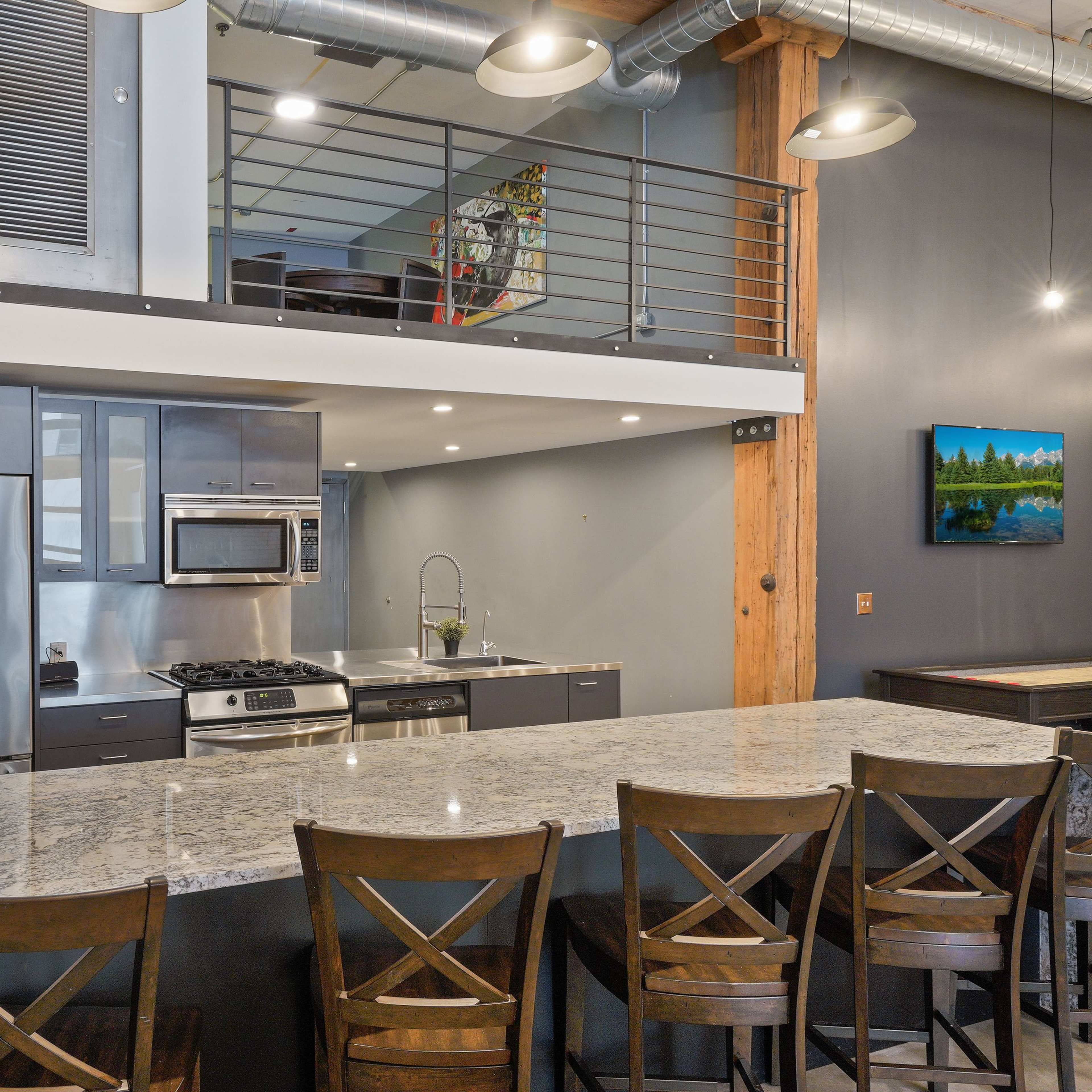 A modern kitchen with stainless steel appliances, a granite countertop, and a second-level balcony visible in the background.