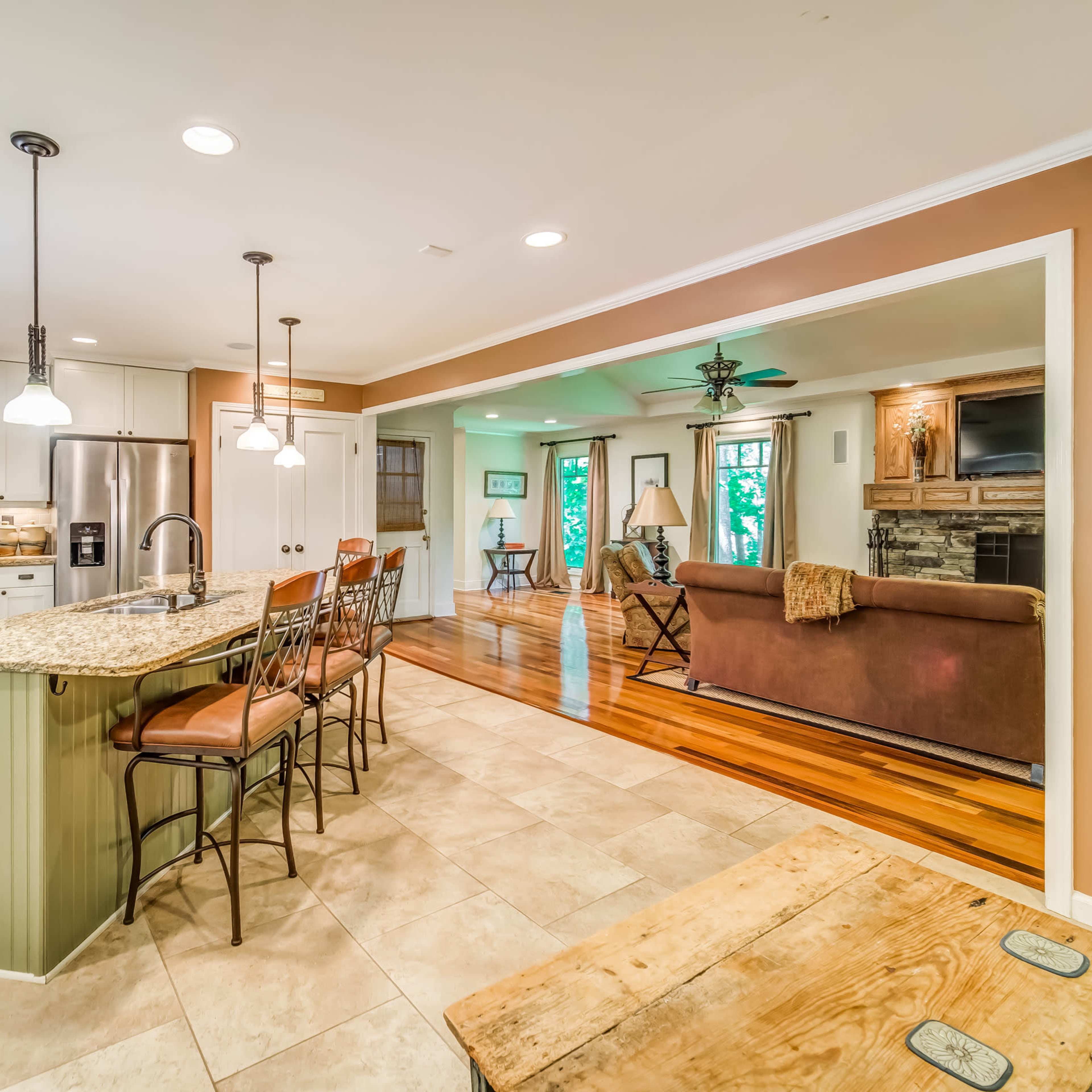 An open kitchen and living area with a granite countertop island, tiled flooring, and wooden accents.