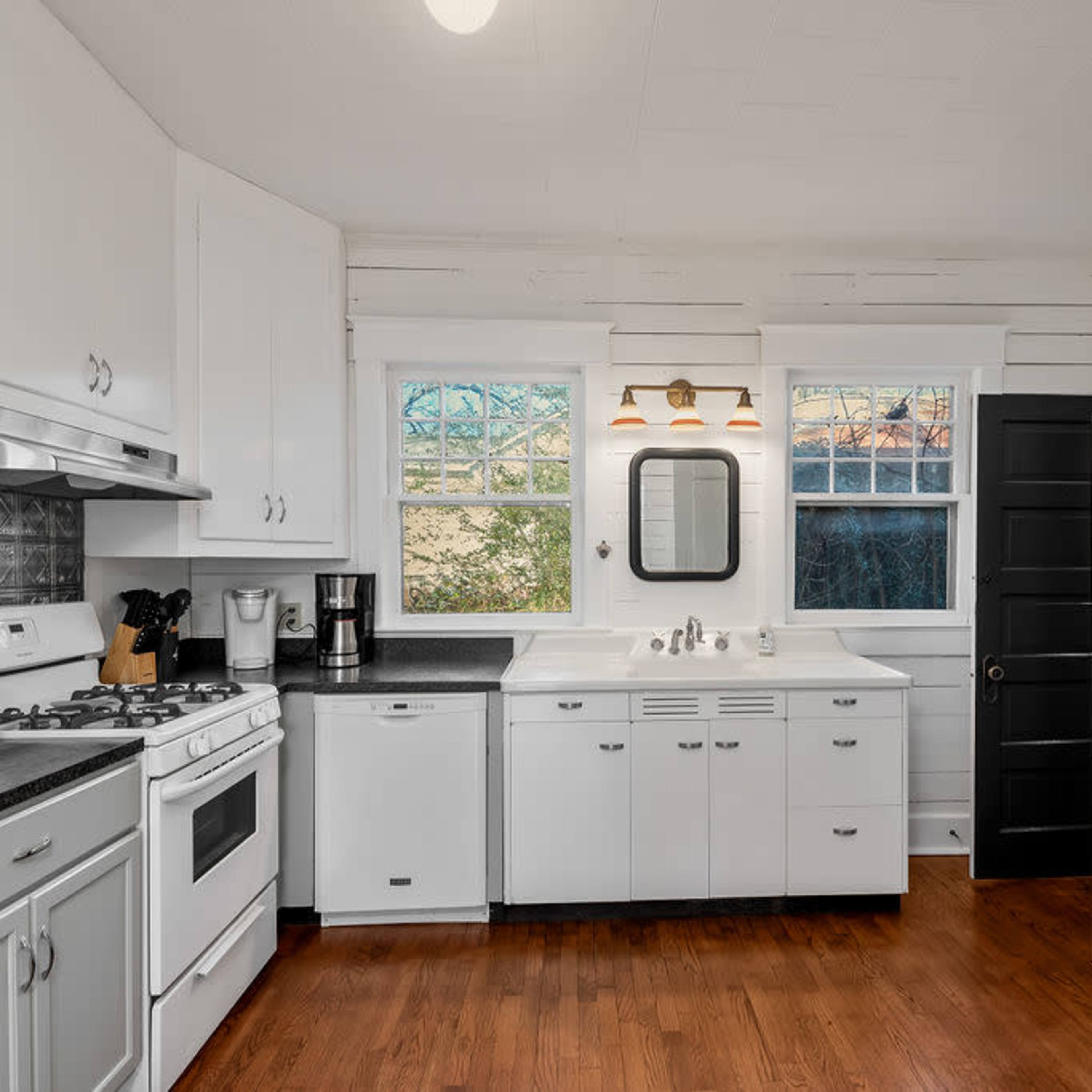 The kitchen features white cabinetry, a black countertop, and a refrigerator, with large windows that allow natural light to enter the space.