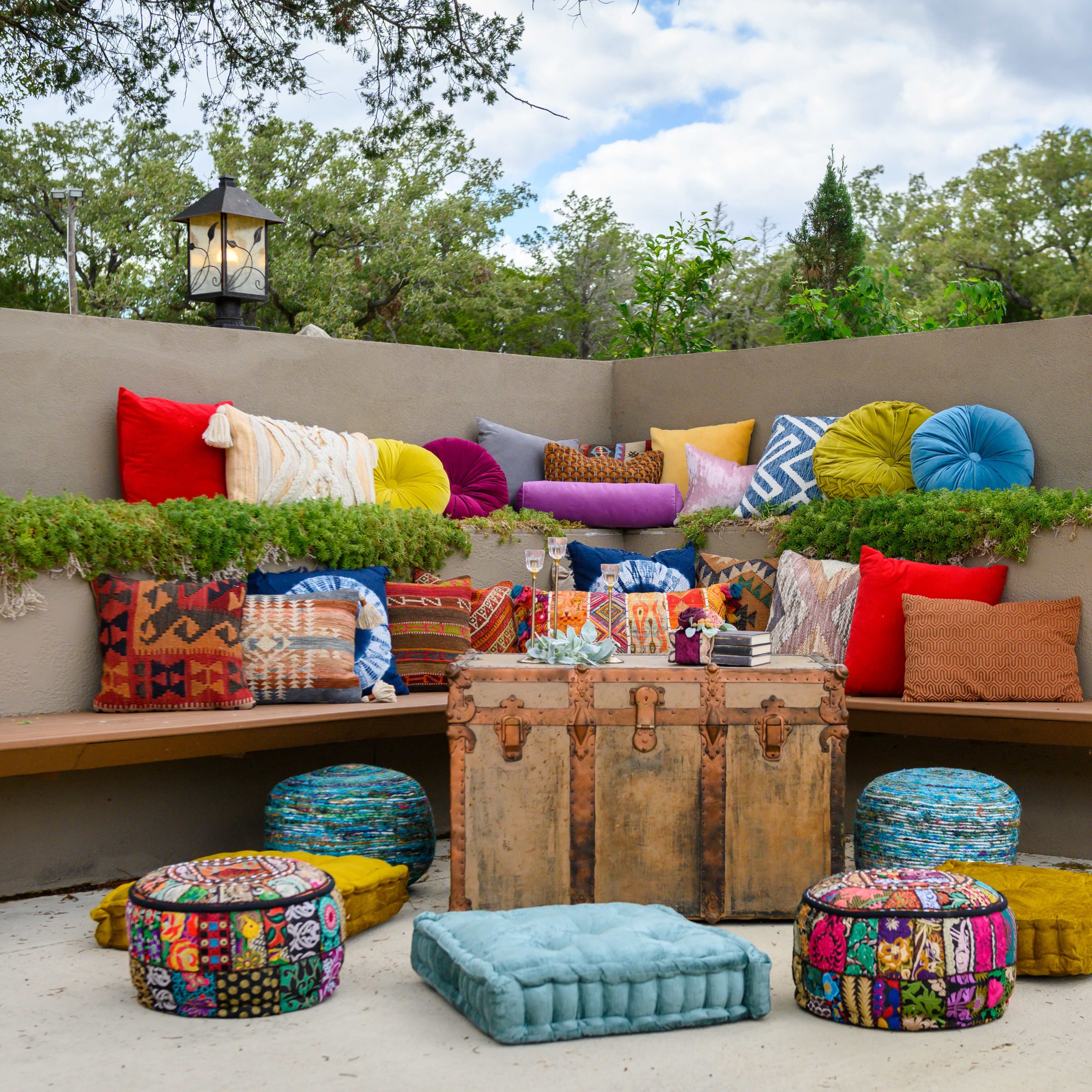 A colorful outdoor seating area with various patterned cushions arranged around a rustic wooden crate.