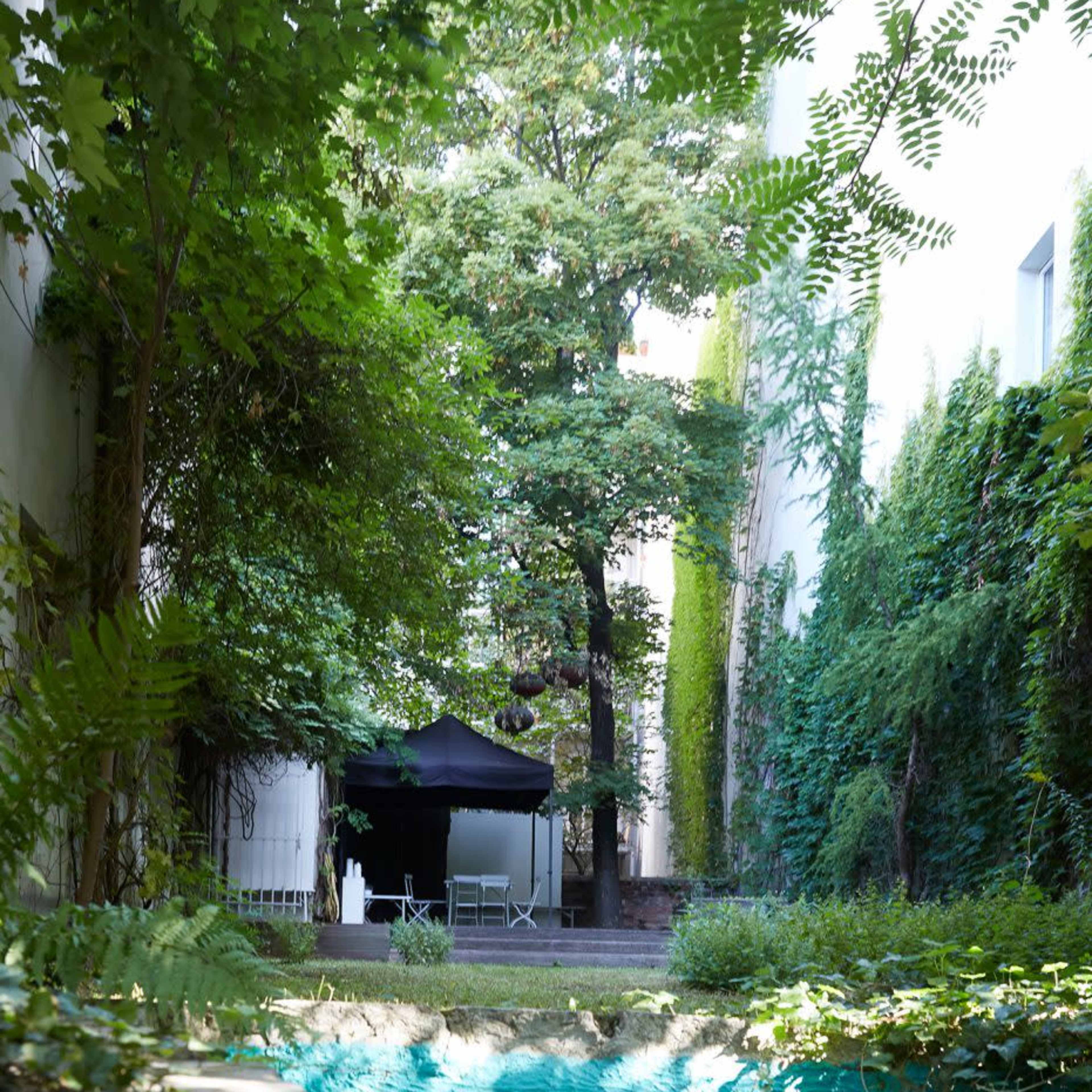 A small outdoor area features a black canopy tent surrounded by lush greenery and a large tree.