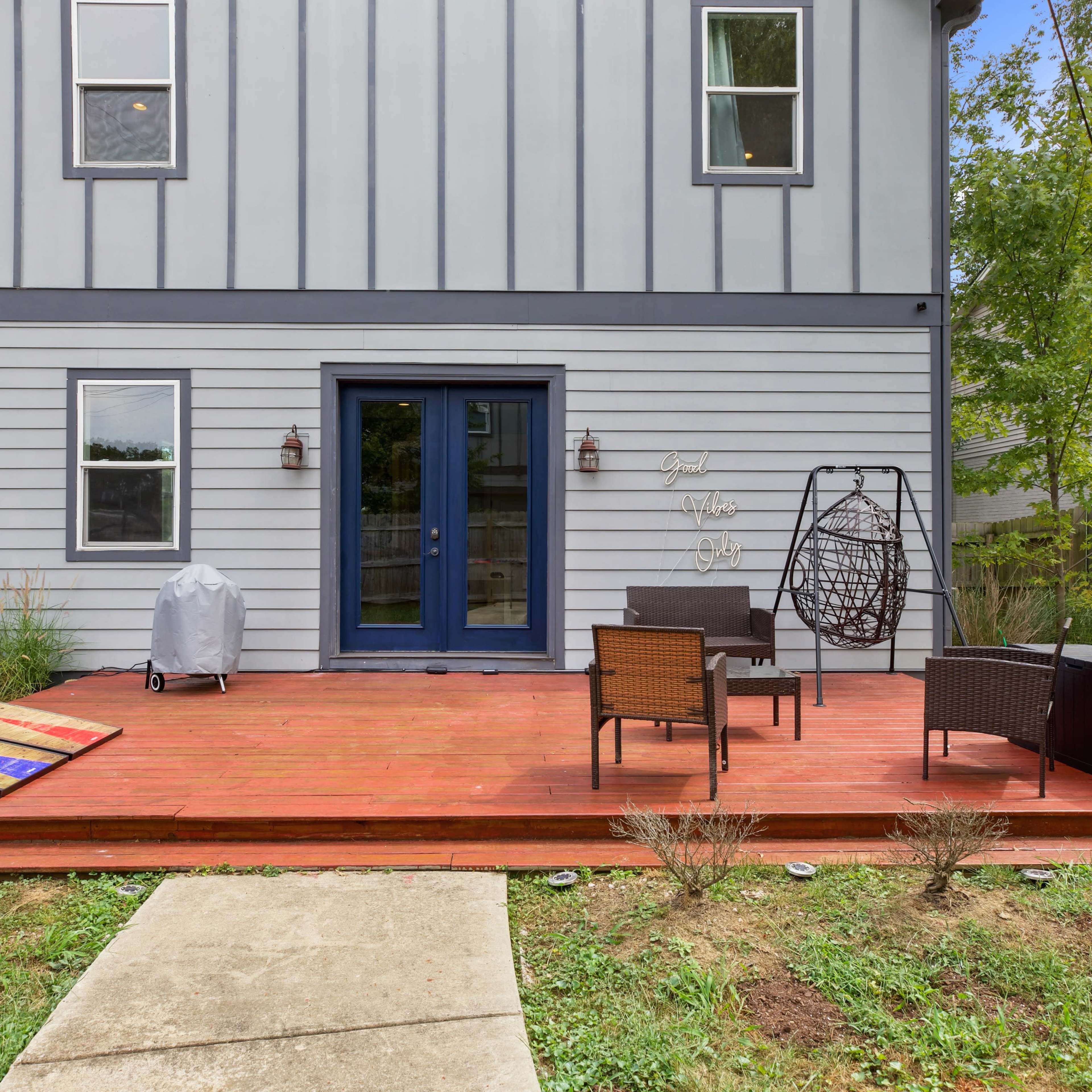 A wooden deck at the back of a house, featuring seating arrangements and a grill.