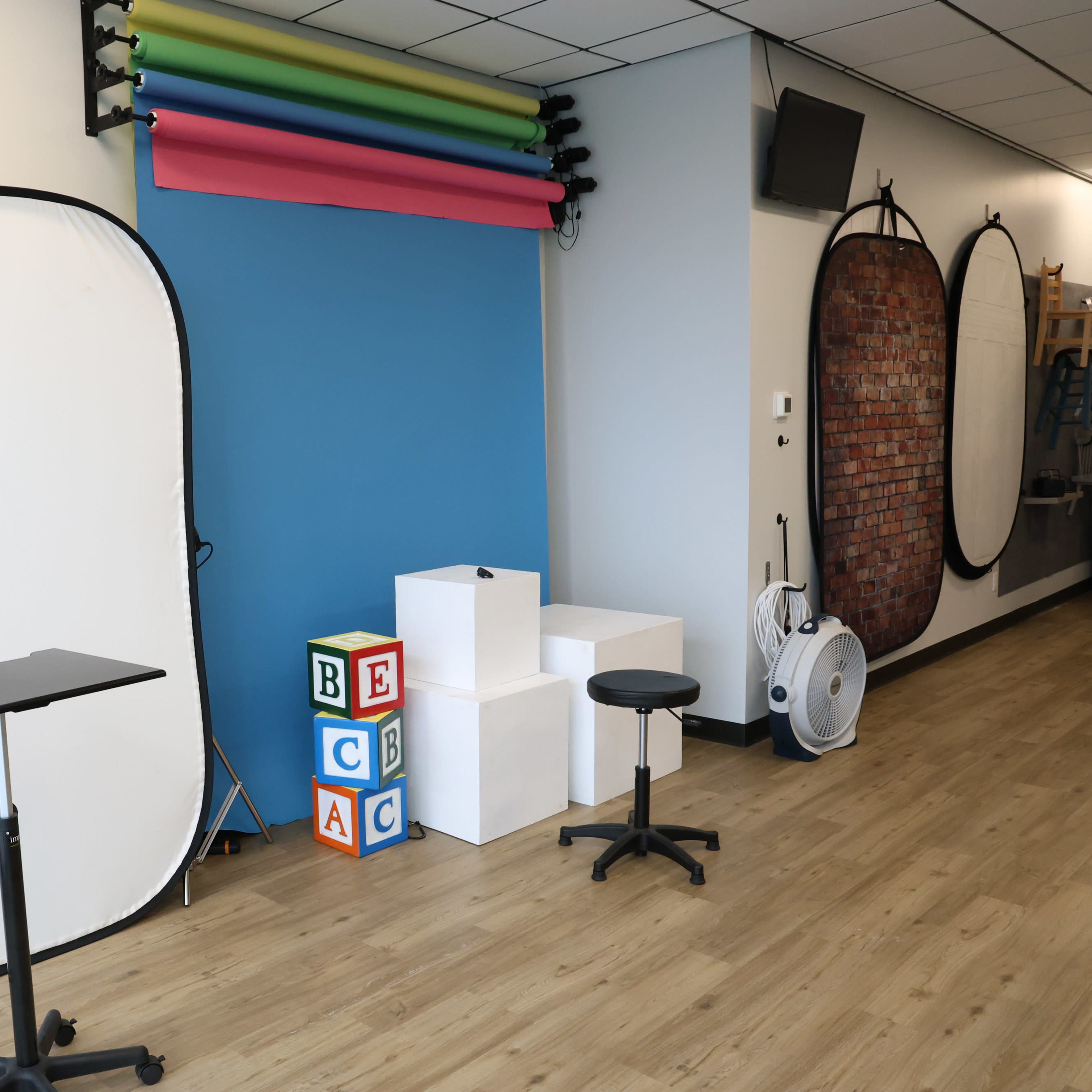 A studio setup with a white backdrop, colorful paper rolls, decorative blocks, and two stools arranged in a well-lit room.