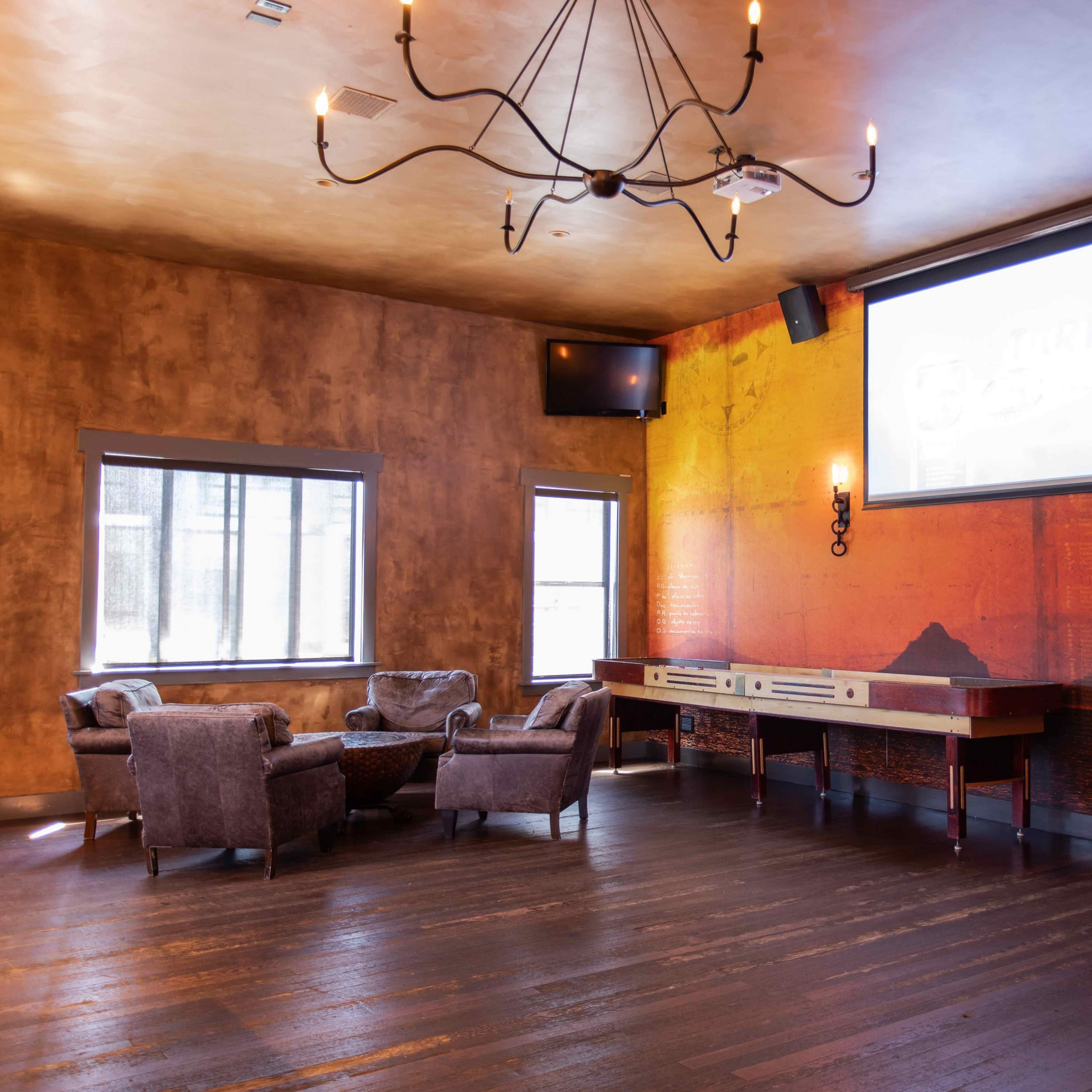 A modern lounge area with two plush armchairs facing a wooden console beneath a large screen, set against a textured wall featuring an orange and black mural.