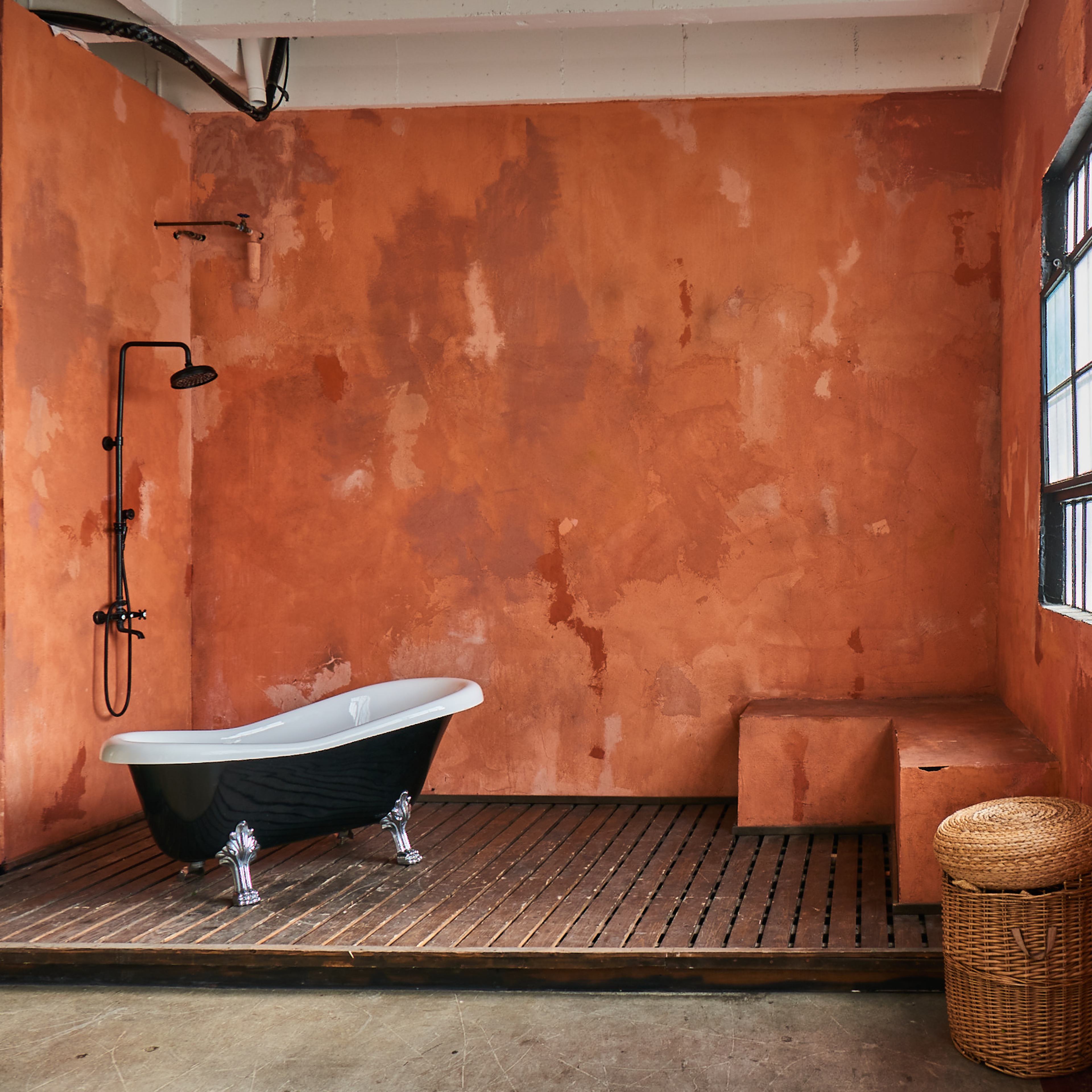 A bathroom with an orange wall, a black freestanding bathtub, a shower fixture, and a woven basket near the window.