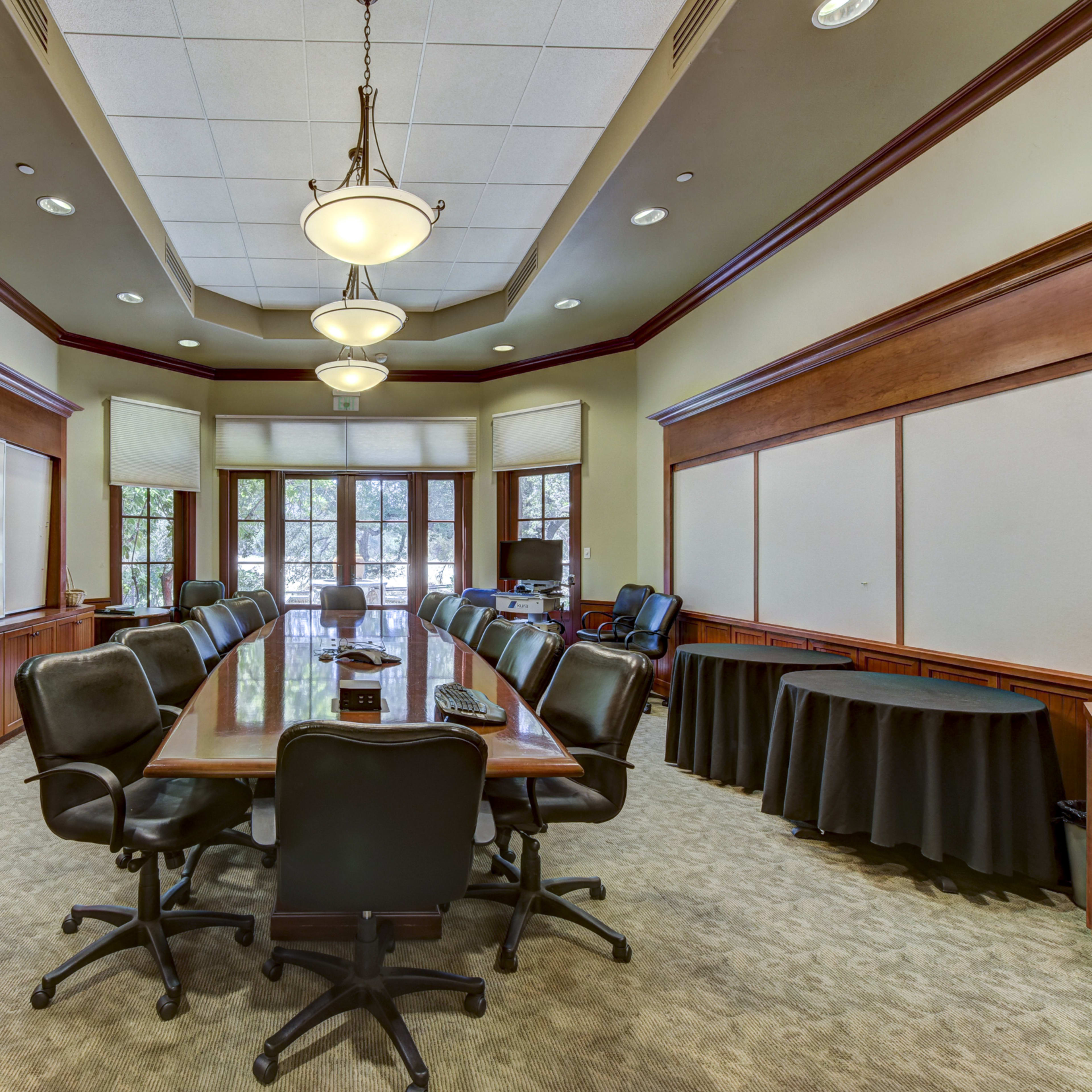 A well-furnished conference room with a large wooden table surrounded by black office chairs and whiteboards on the walls.