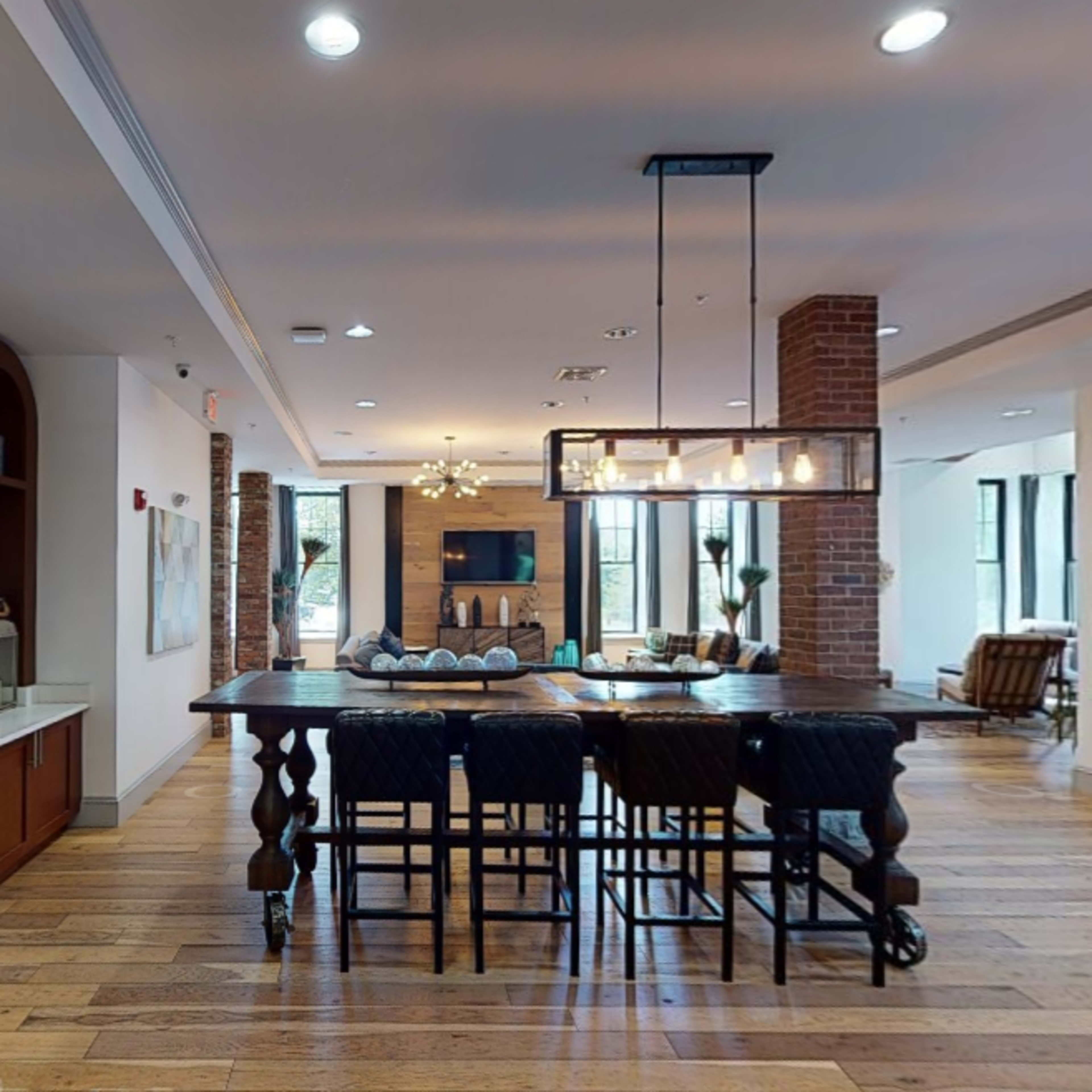 A modern interior space with a coffee station, a large dining table surrounded by chairs, and a seating area in the background.